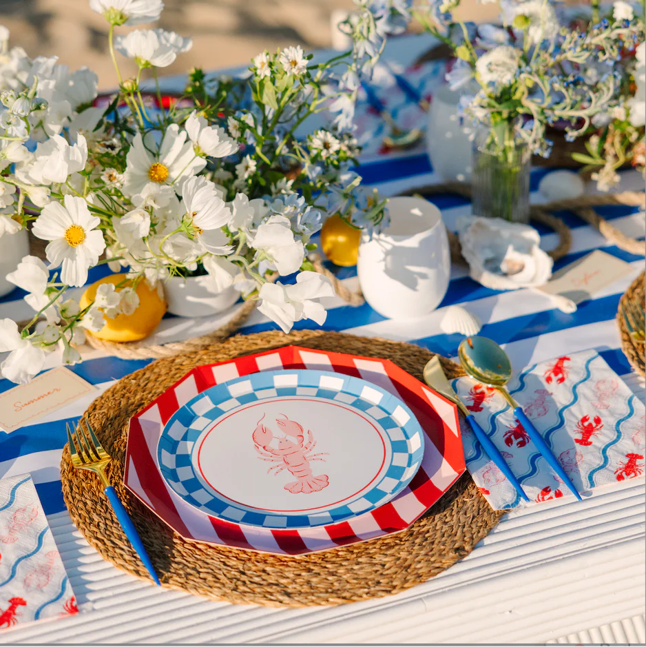Close-up of lobster paper plate on rattan charger styled at a coastal summer table setting with lobster napkins and white wildflowers