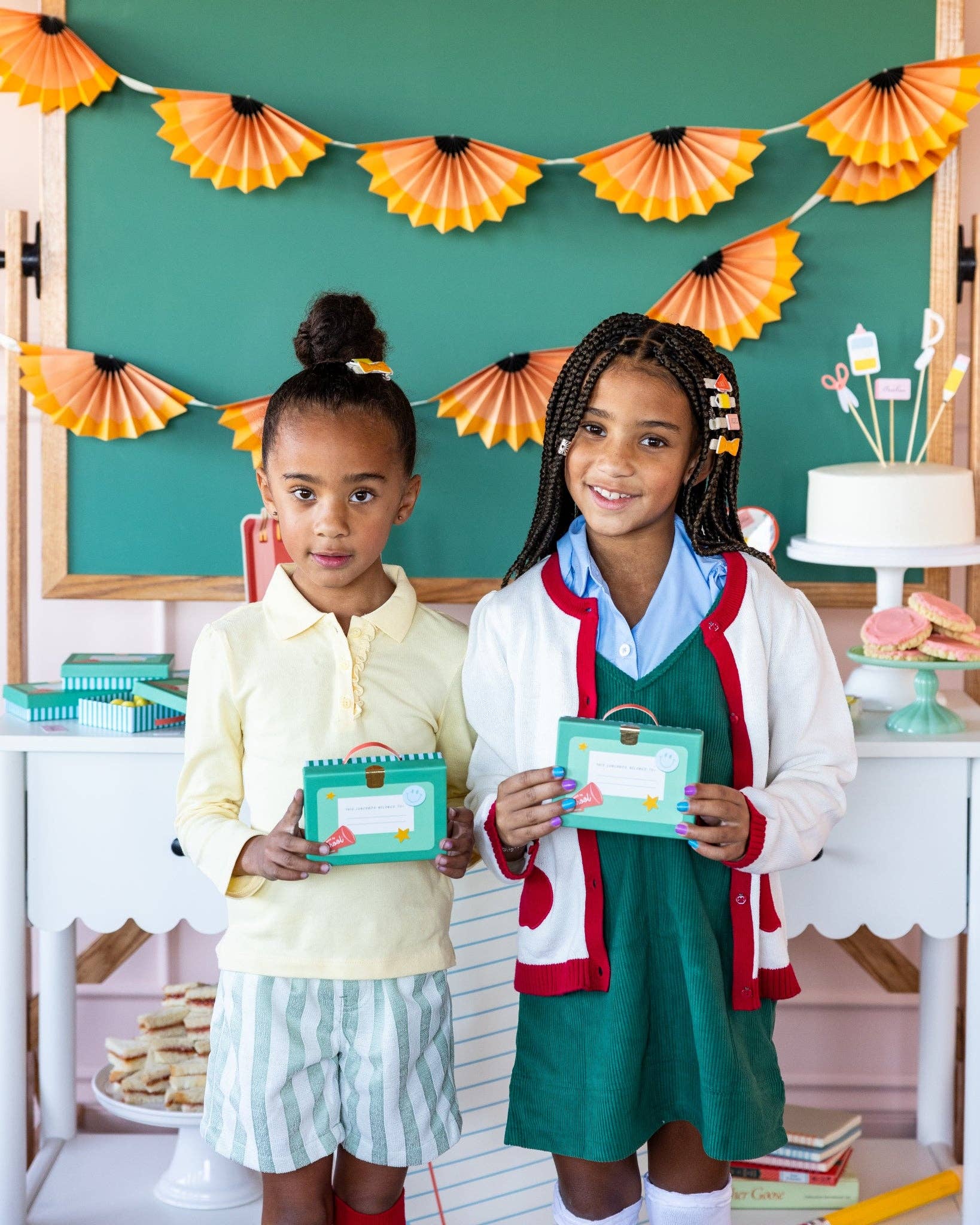 Two children holding teal lunchbox shaped treat boxes with ribbon handles at styled back to school party table