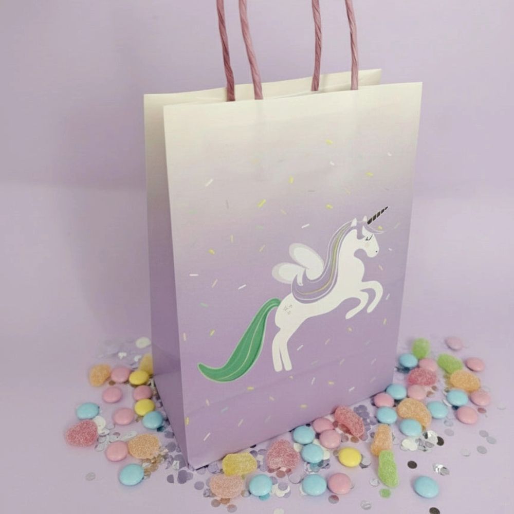 Side view of a unicorn gift bag surrounded by pastel candies and glitter