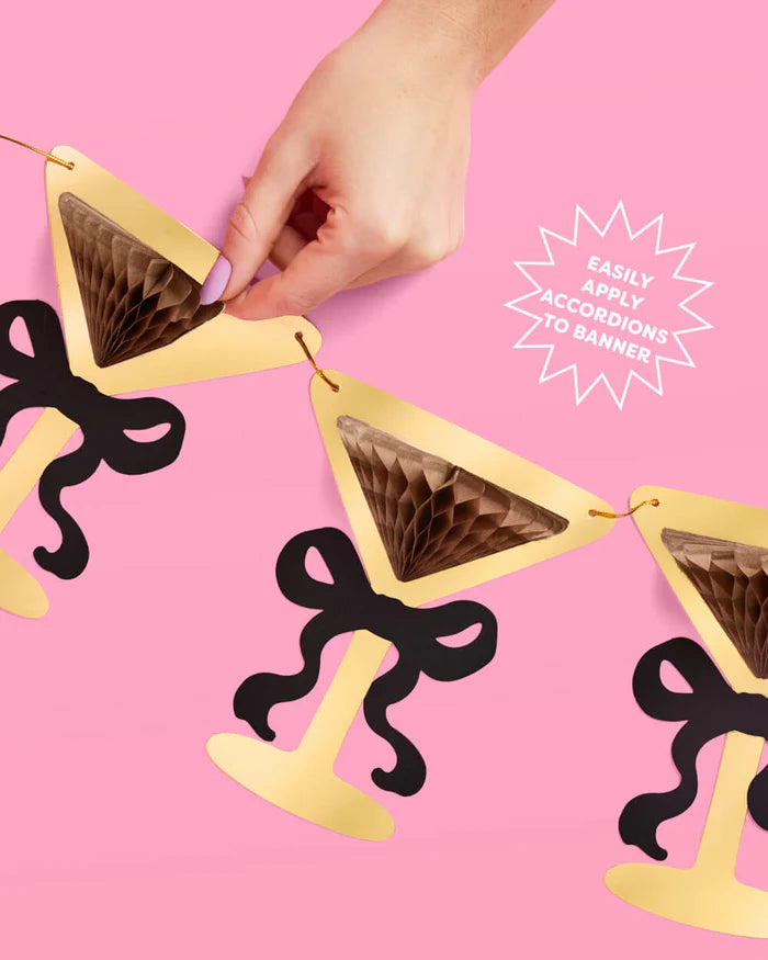Hand opening brown tissue accordion on gold foil martini glass banner piece, with callout reading "easily apply accordions to banner"