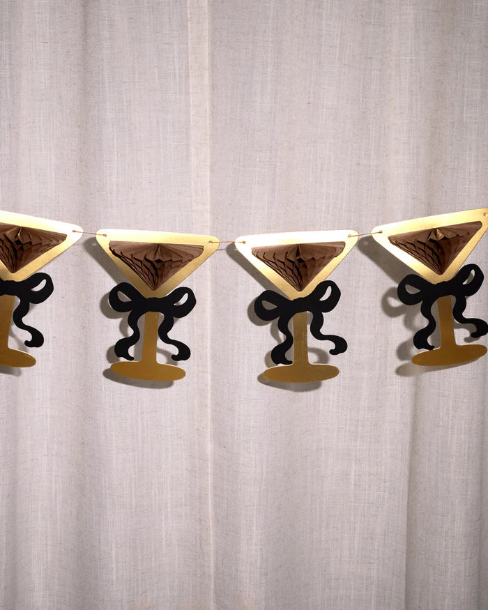 Close-up of four gold foil martini glasses with black bows against white linen curtain