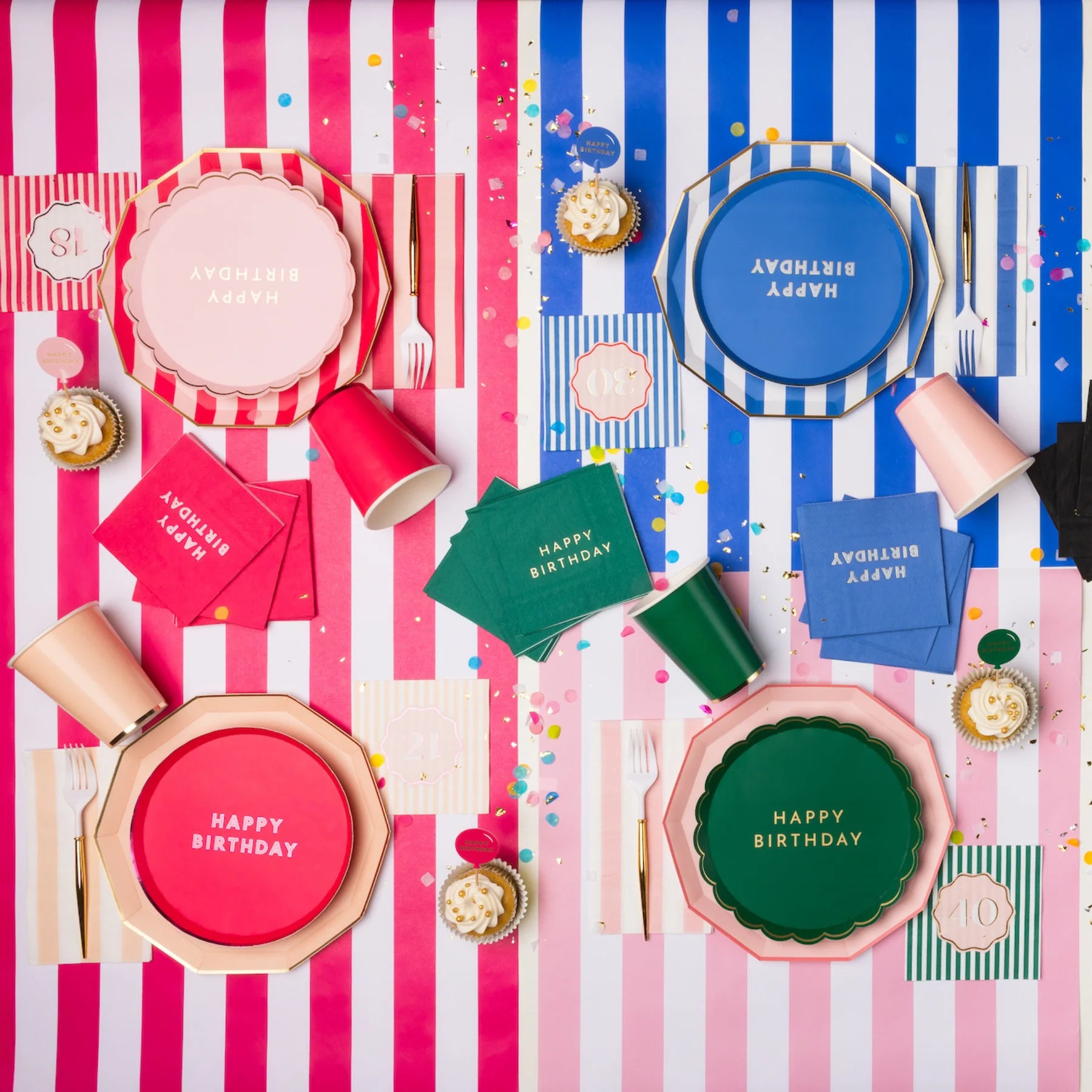 Overhead lifestyle shot of colorful milestone birthday party table with assorted Happy Birthday plates, napkins and cups in pink, blue and green on striped tablecloths with confetti
