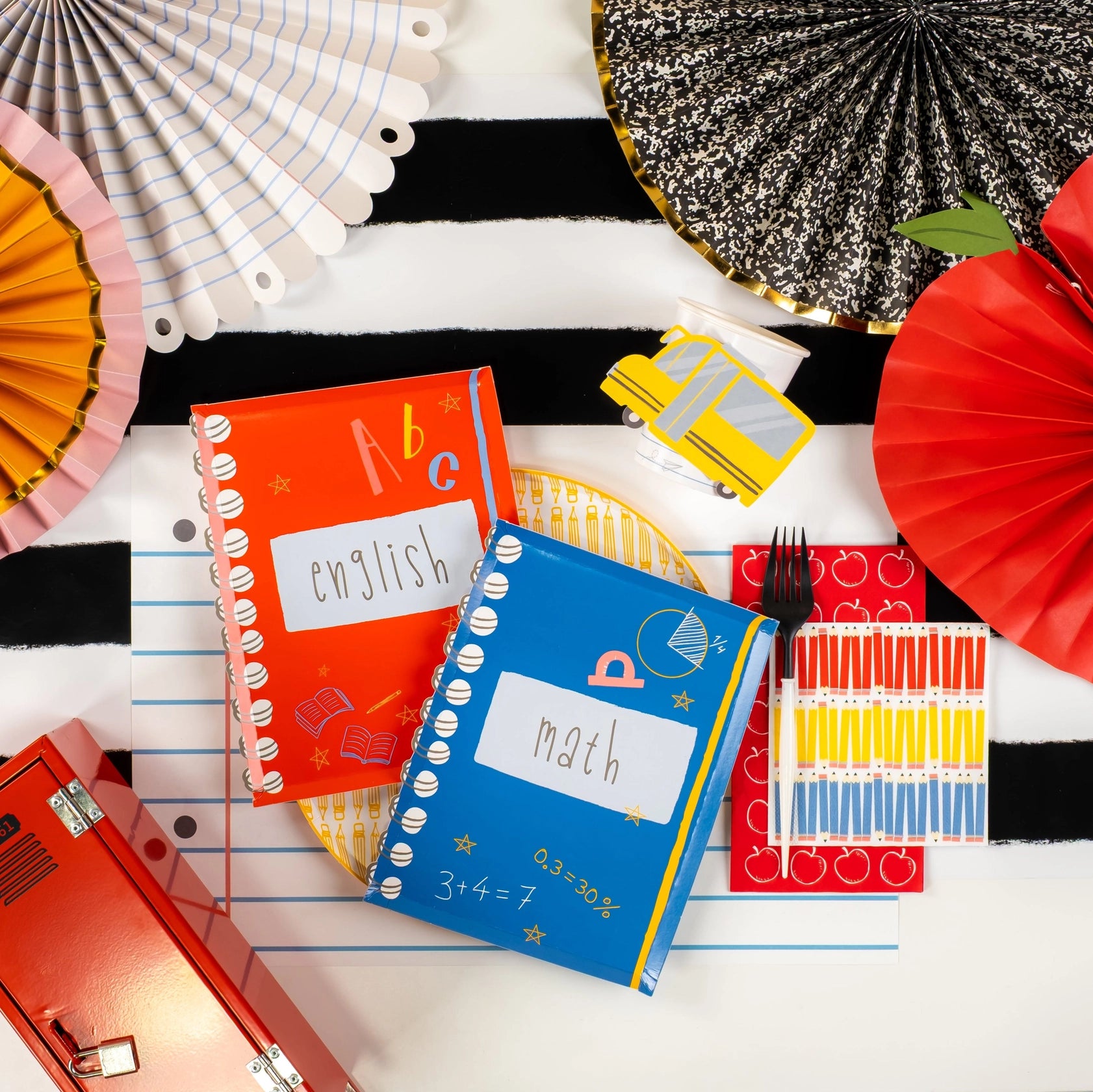 Flat-lay of school-themed party supplies featuring apple guest towel and notebooks.
