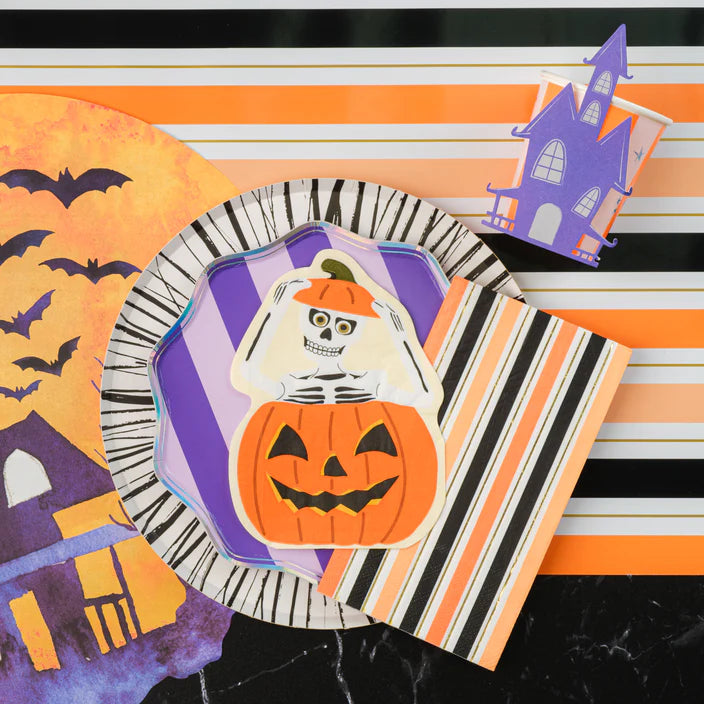 Flat lay with skeleton pumpkin plate, striped napkin, and haunted house cup on black stripe runner.