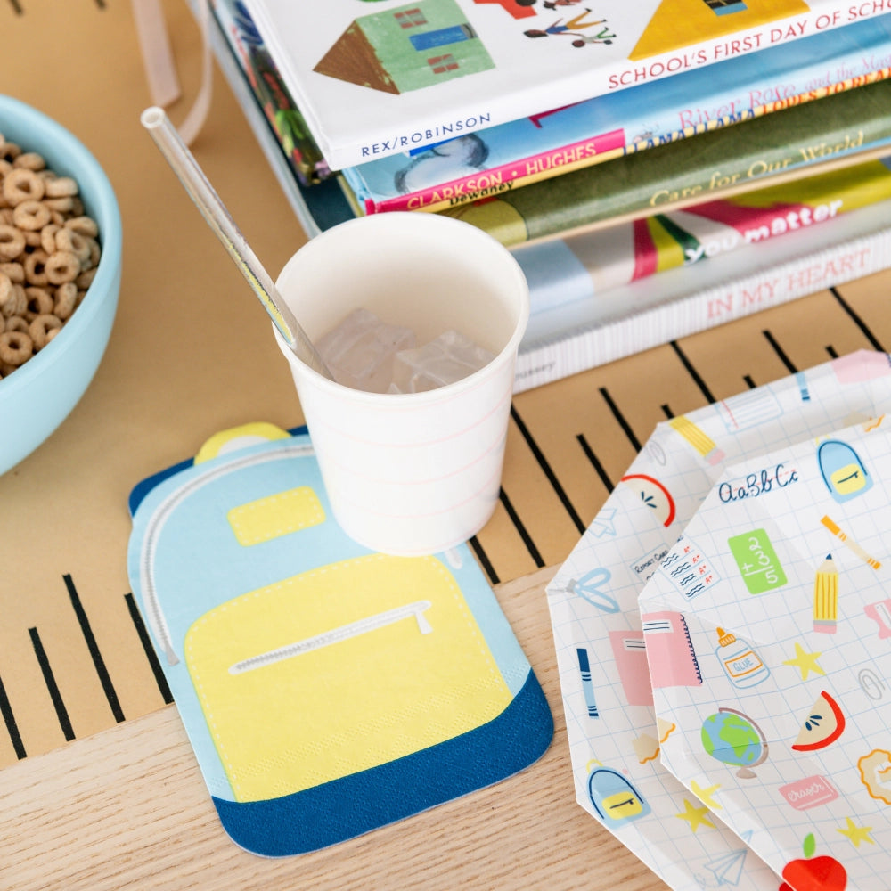 Backpack napkin used as coaster beside cup and school books in breakfast scene	