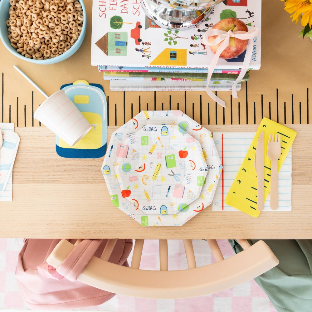 Overhead table setting with backpack napkin under cup next to school-supply plates	