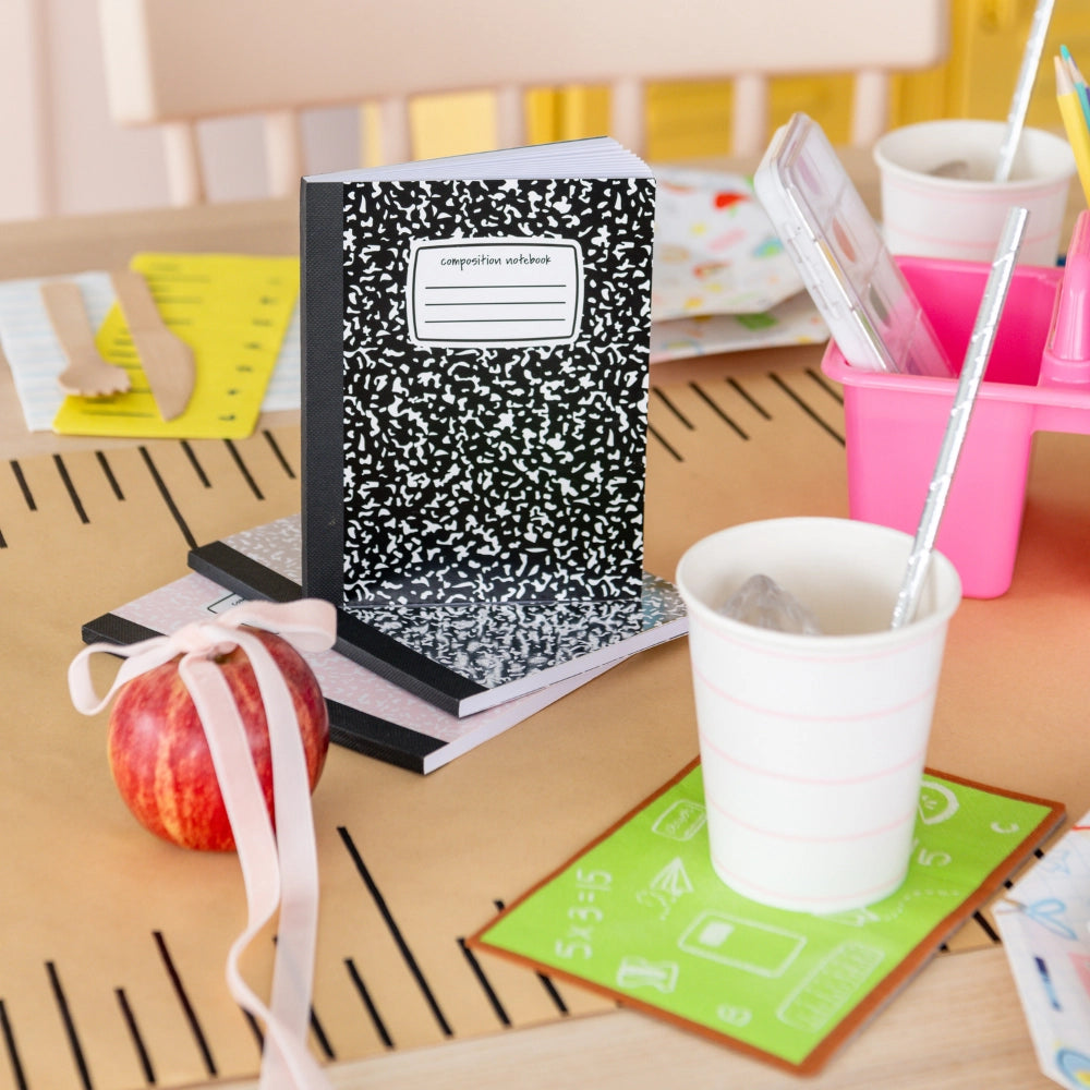 Side view of chalkboard napkin used as coaster beside composition notebook stack, apple, and cups with silver straws