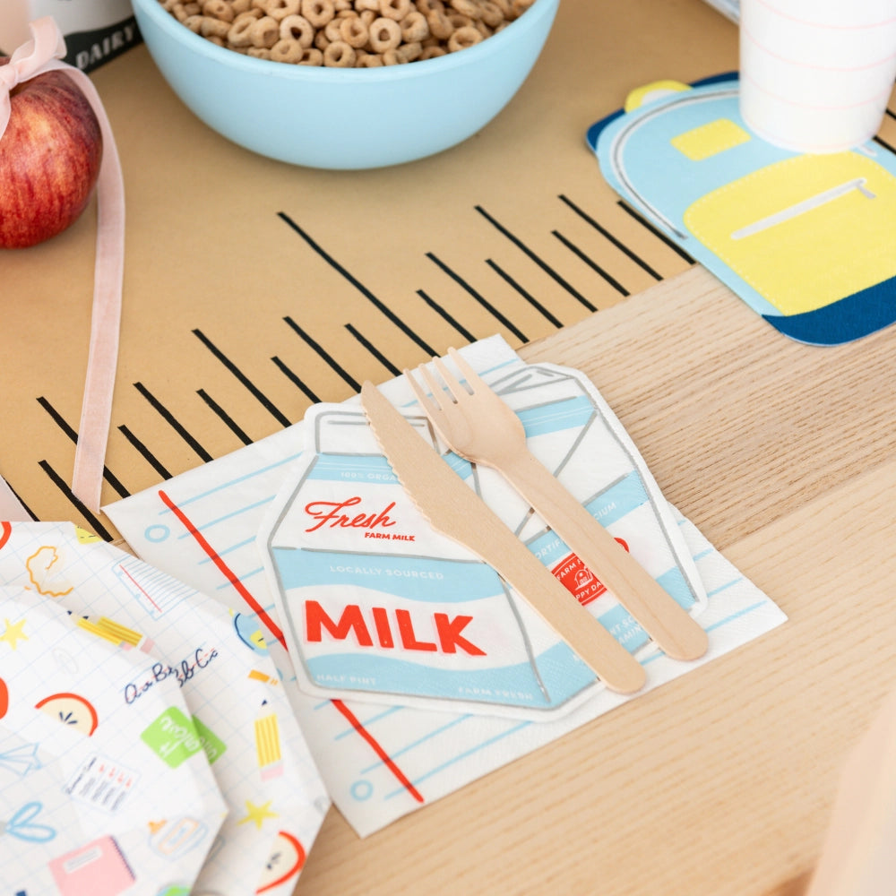 Close-up of milk-carton napkin atop notebook-paper napkin next to backpack coaster and cereal bowl for themed back to school party