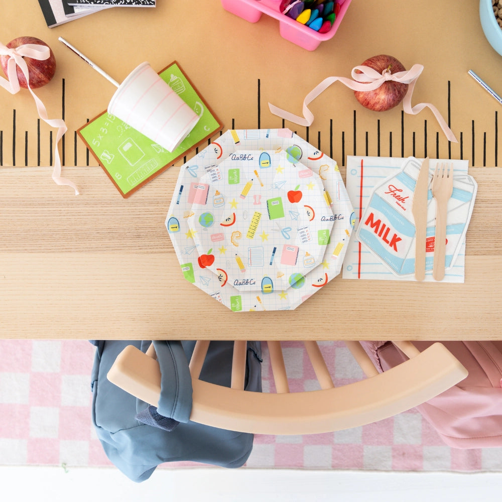 Styled breakfast table featuring milk-carton napkin layered on notebook napkin with wooden utensils and ruler runner