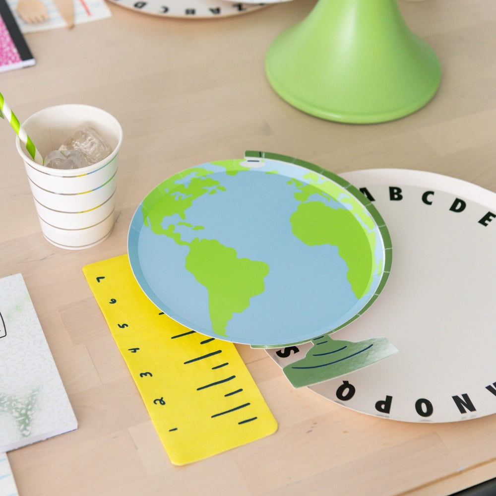 Snack station featuring globe plate resting partly on ruler napkin, striped cup with ice, and math notebook for themed back to school decorations	