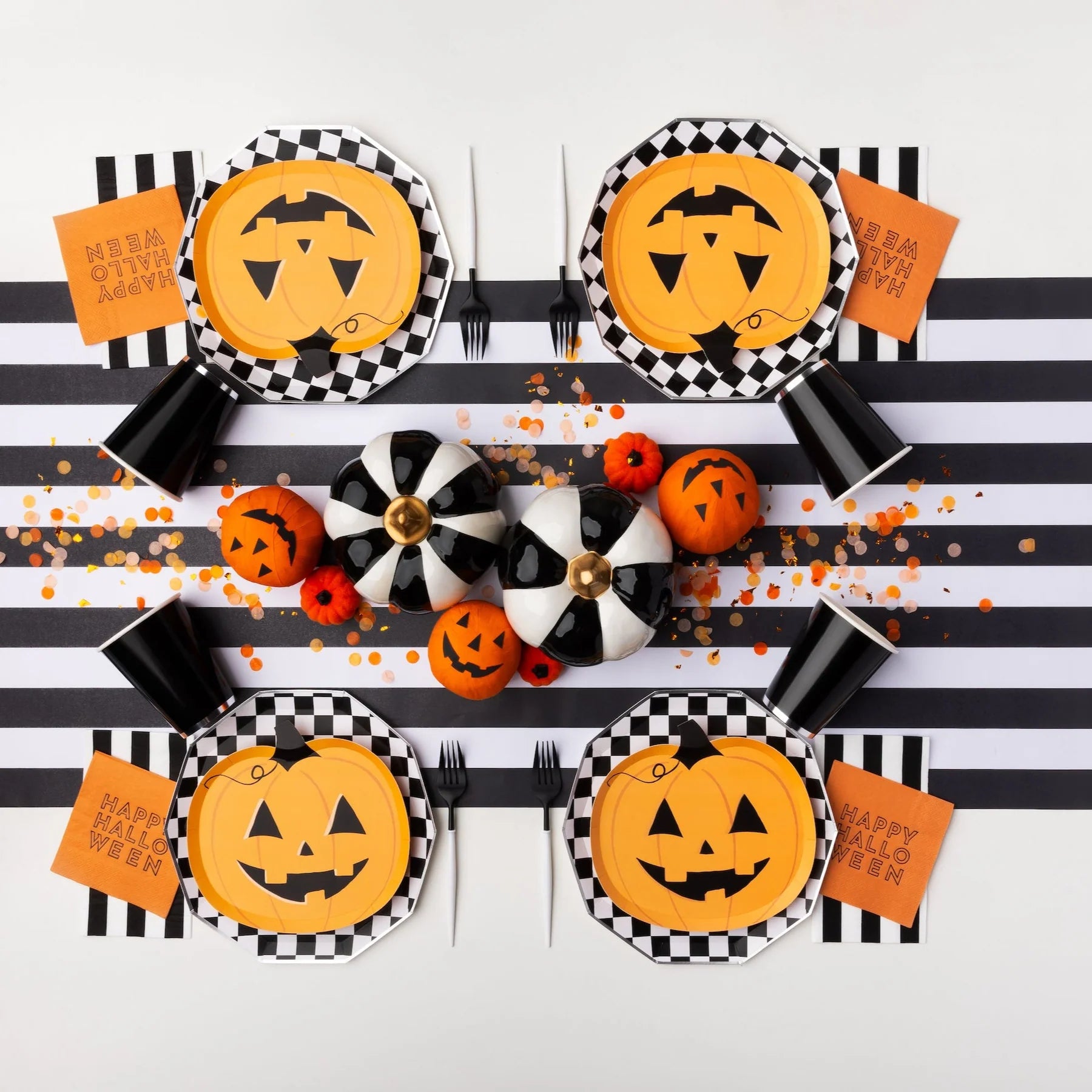 Overhead tablescape with checkerboard chargers and jack-o-lantern pumpkin paper plates, bold Halloween plates look