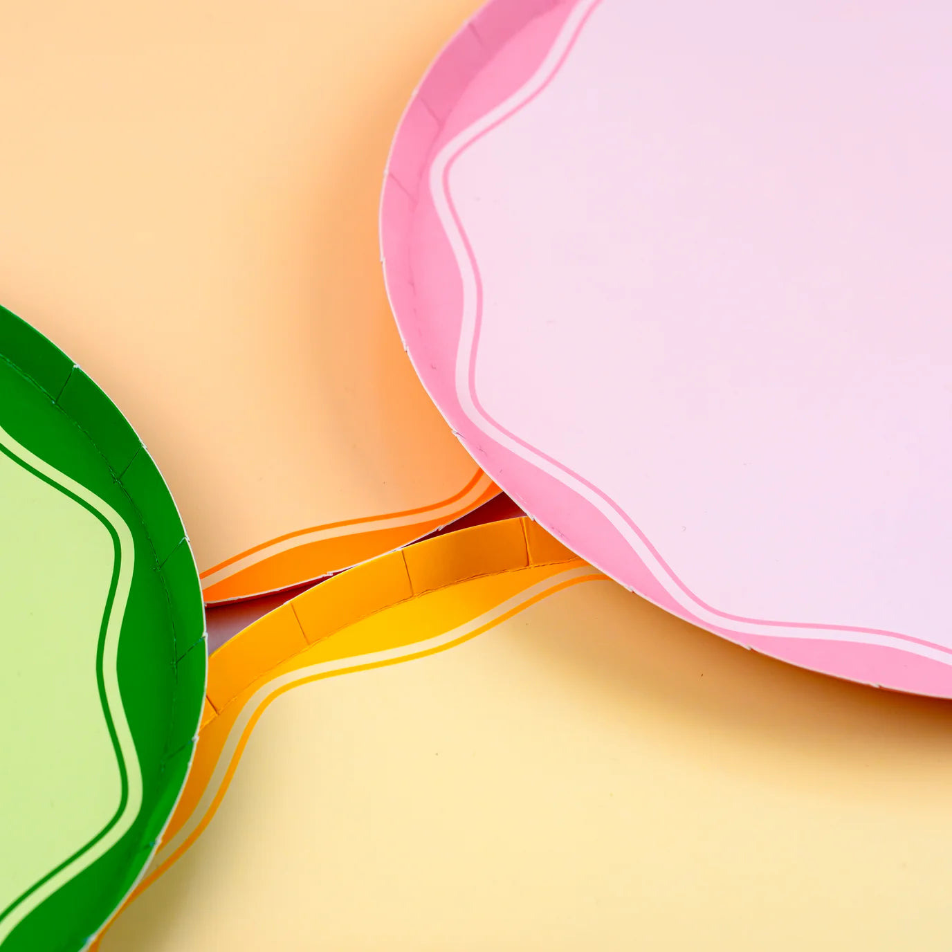 Close up of pink paper plates and green plate showing wavy rim on peach background