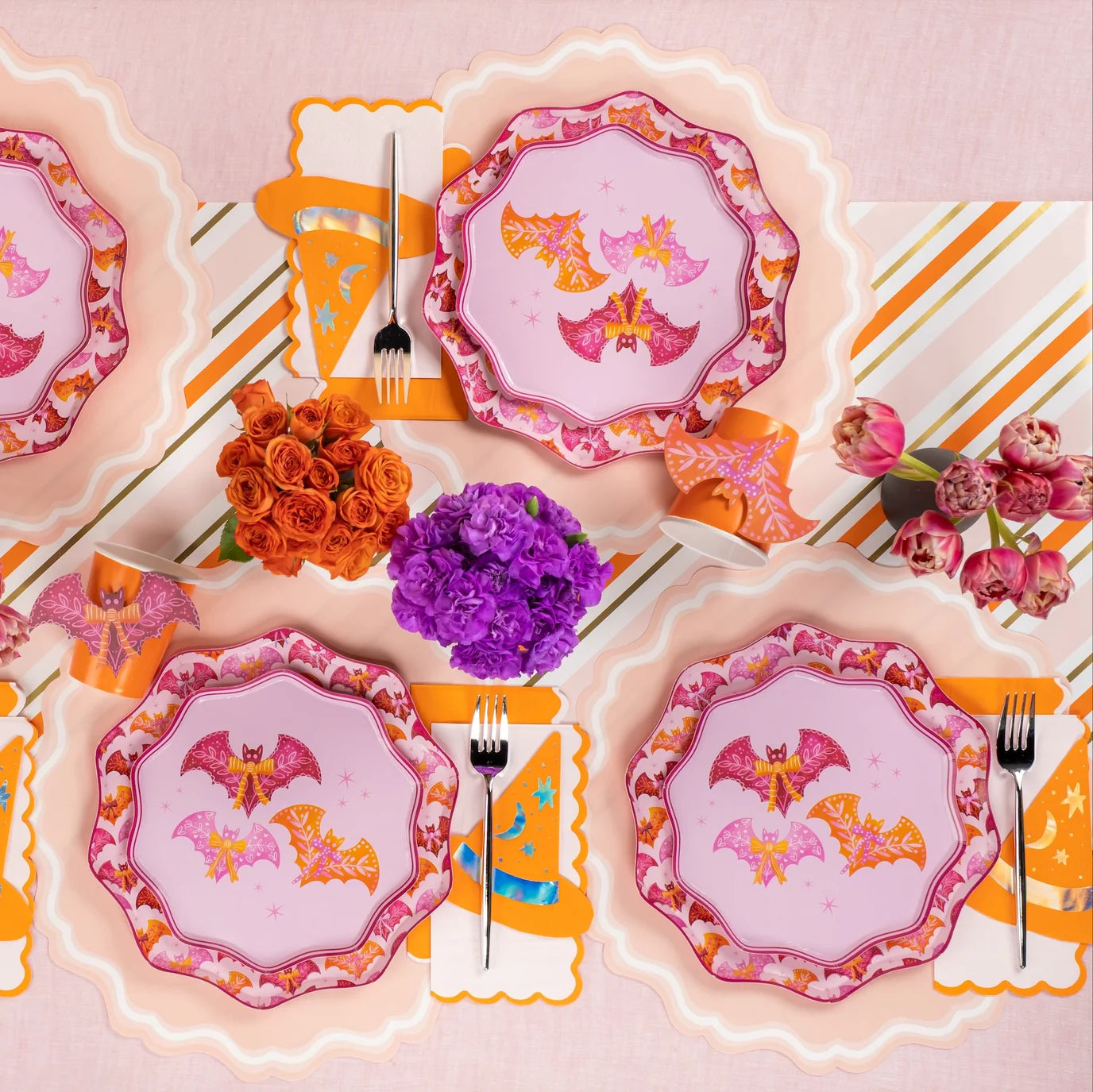 Tablescape with bats and bows plates layered on blush pink placemats, scalloped paper placemats