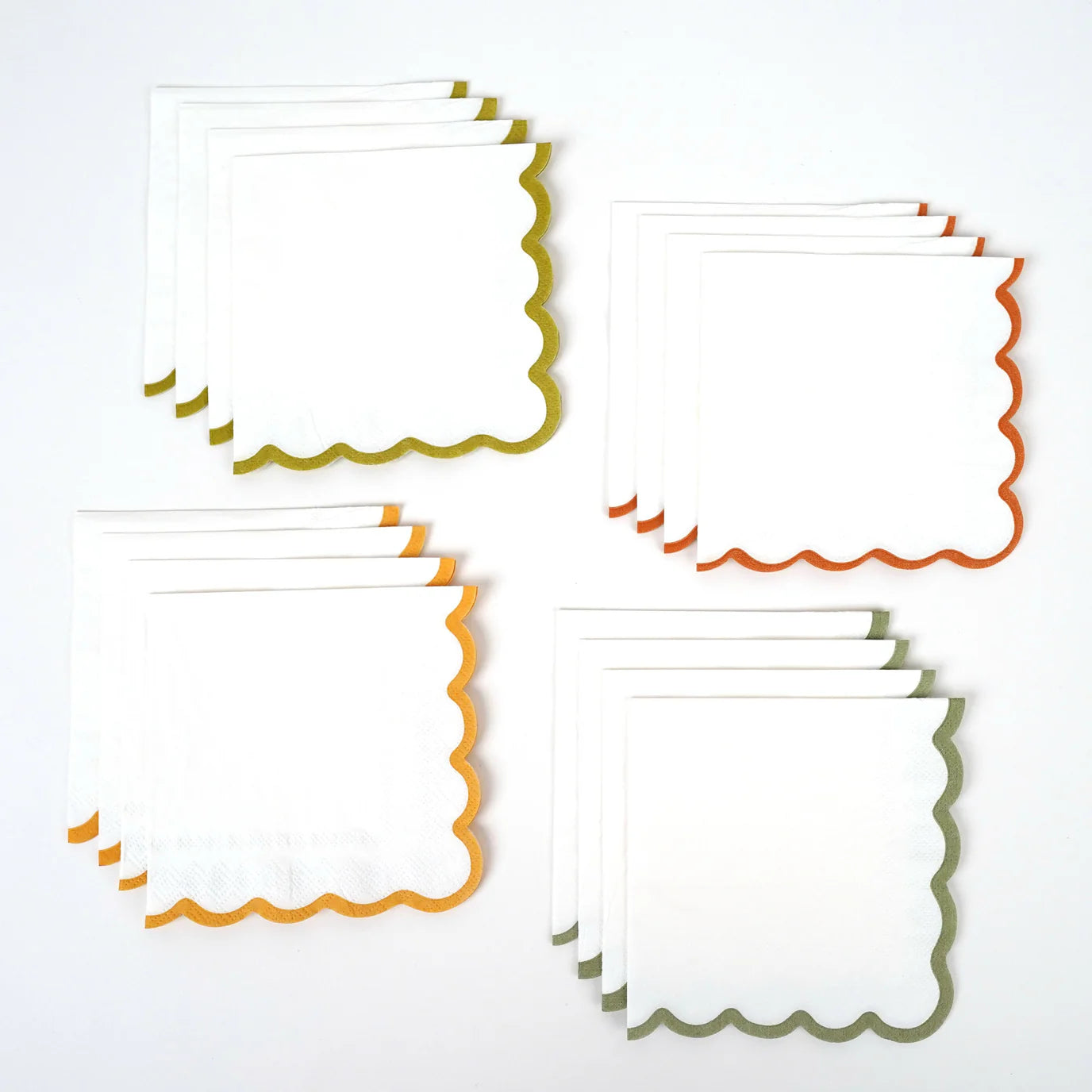 Stacked white scallop paper cocktail napkins with olive, orange, and gold edges