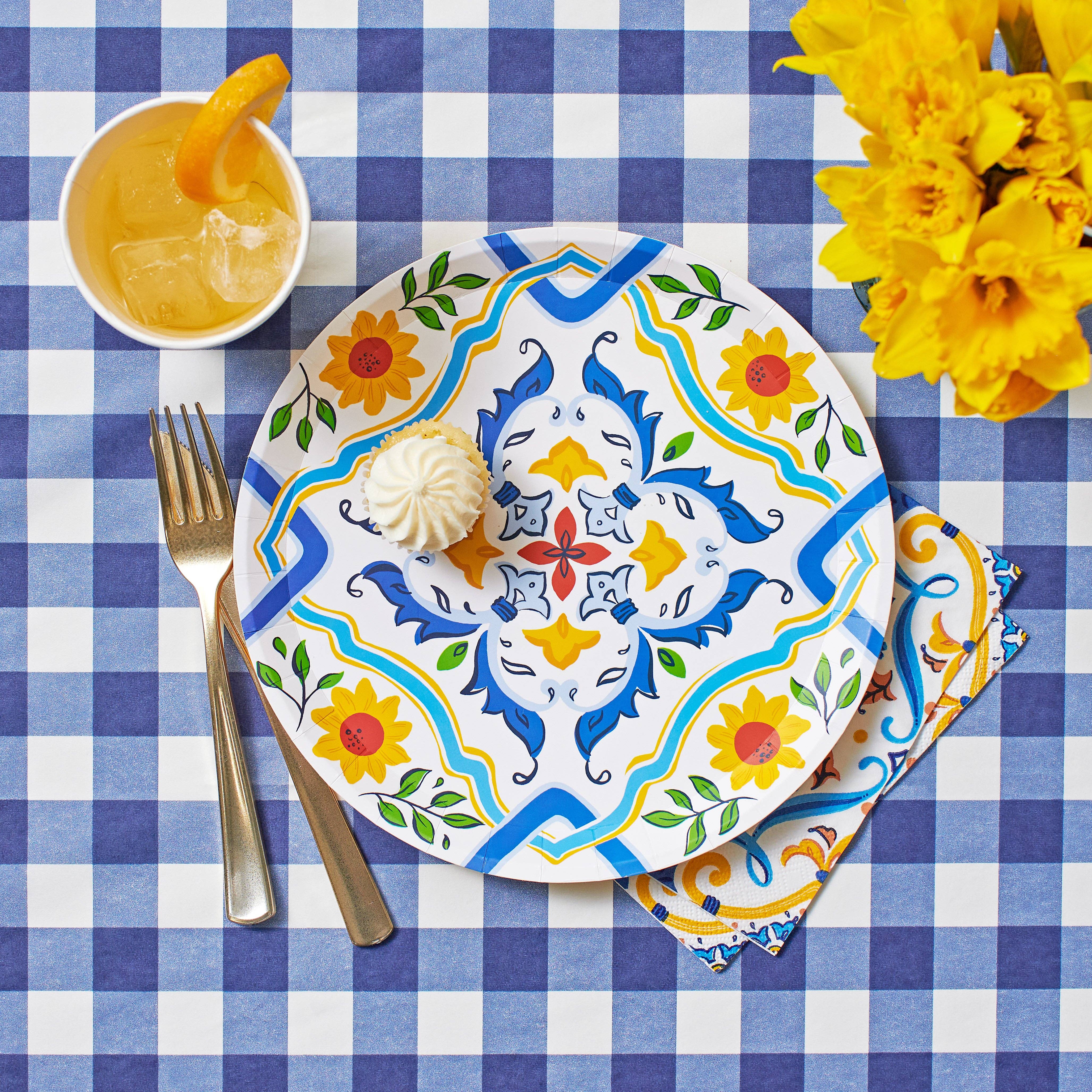 Overhead shot of a navy gingham paper tablecloth styled with a Mediterranean floral plate and yellow flowers.