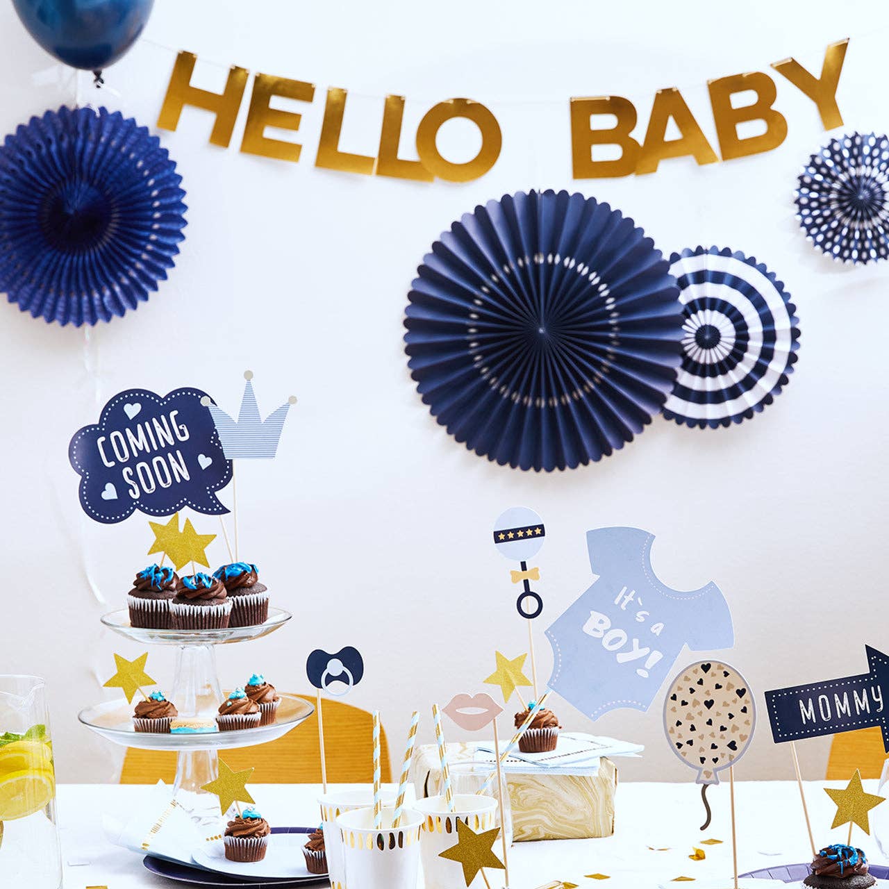 Classic navy and gold baby shower backdrop with navy party fans, "Hello Baby" banner, and "It's a Boy" cupcake display.