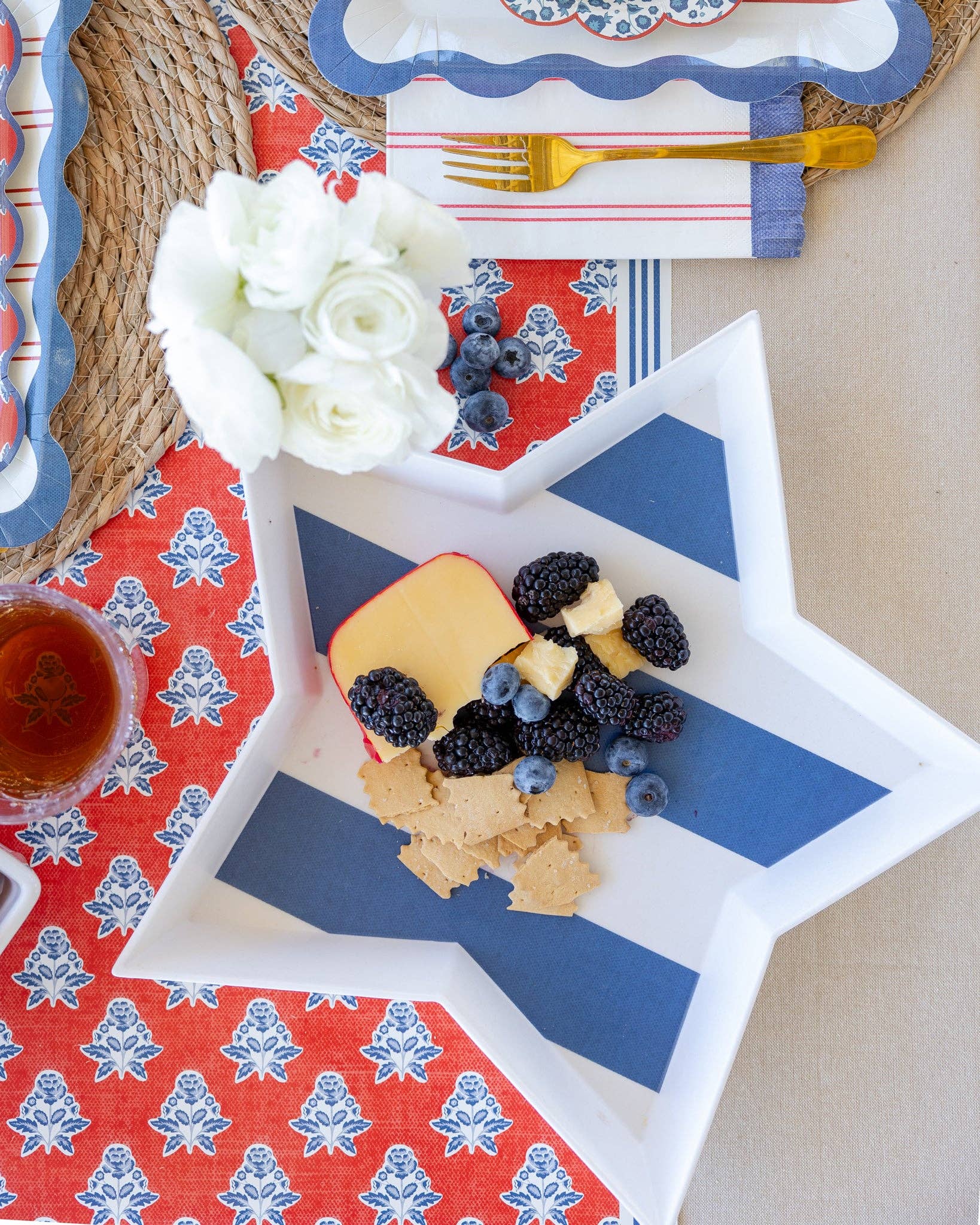 Overhead of navy striped star bamboo tray with cheese and berries on red block print runner