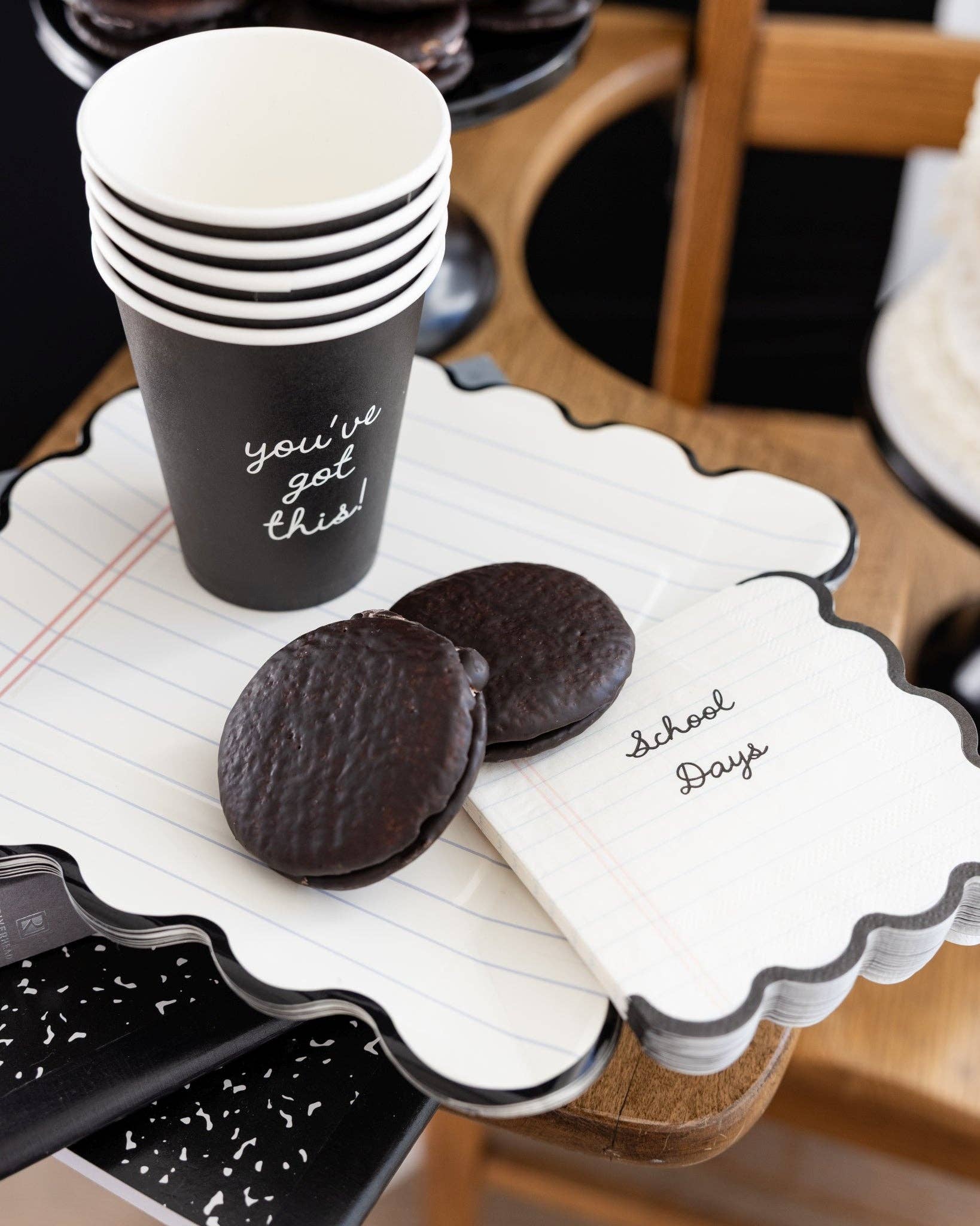 Styled back to school dessert table with notebook paper scalloped plate holding chocolate whoopie pies under a black "you've got this" paper party cup, with School Days notebook paper napkins on top