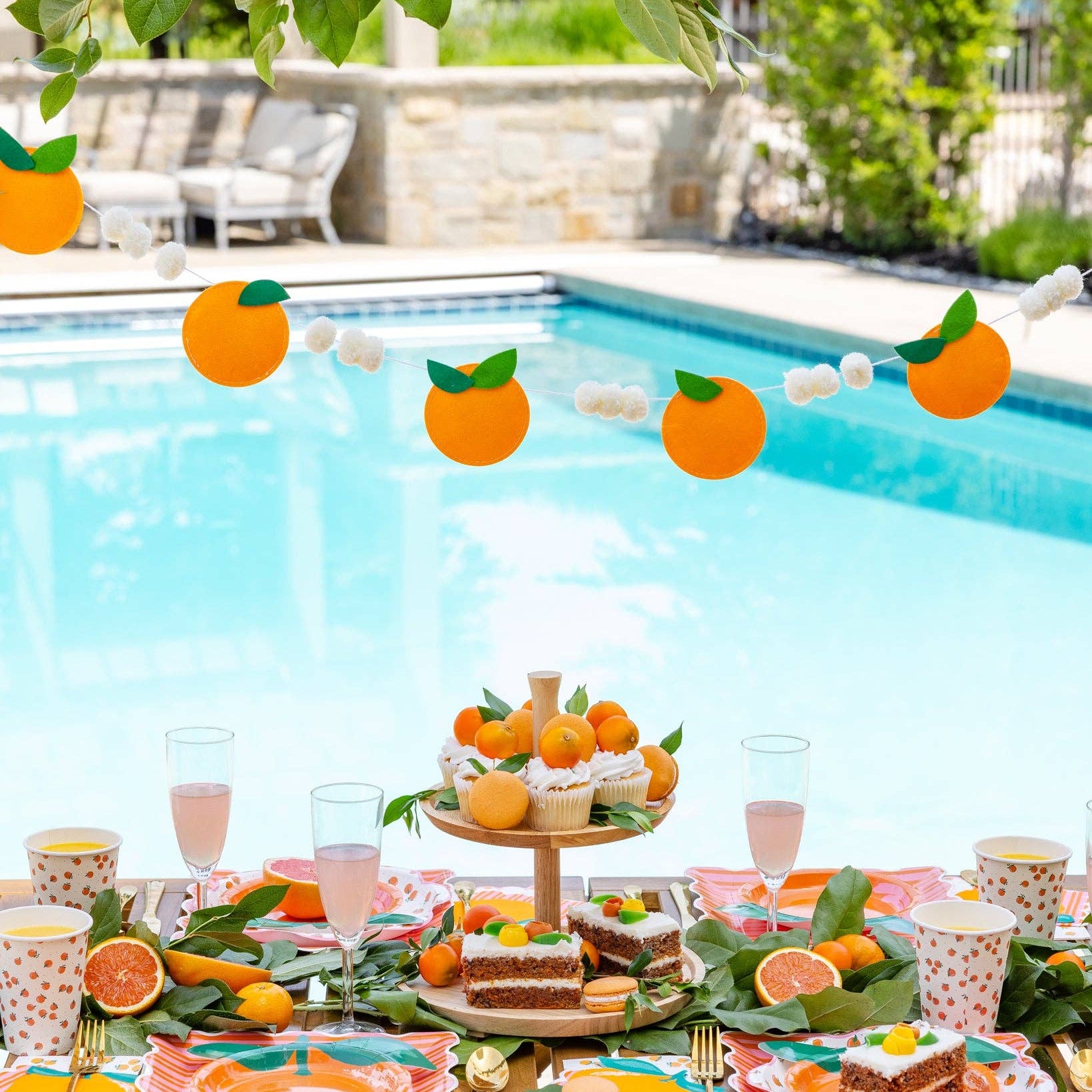 Orange felt garland with pom details above a summer poolside tablescape.