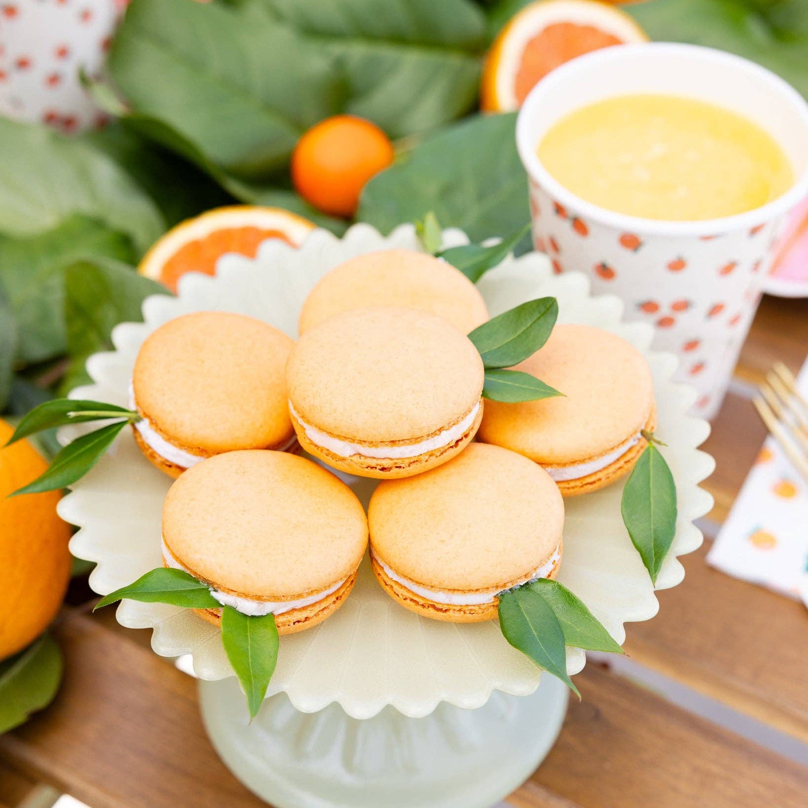 Orange macarons displayed beside matching orange party cups and citrus decor.