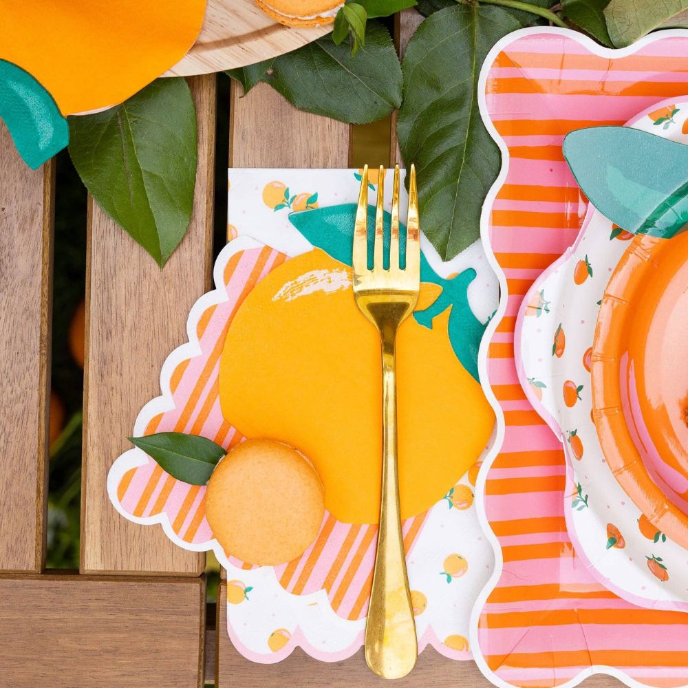 Orange and pink striped cocktail napkin styled with orange party tableware and gold fork.
