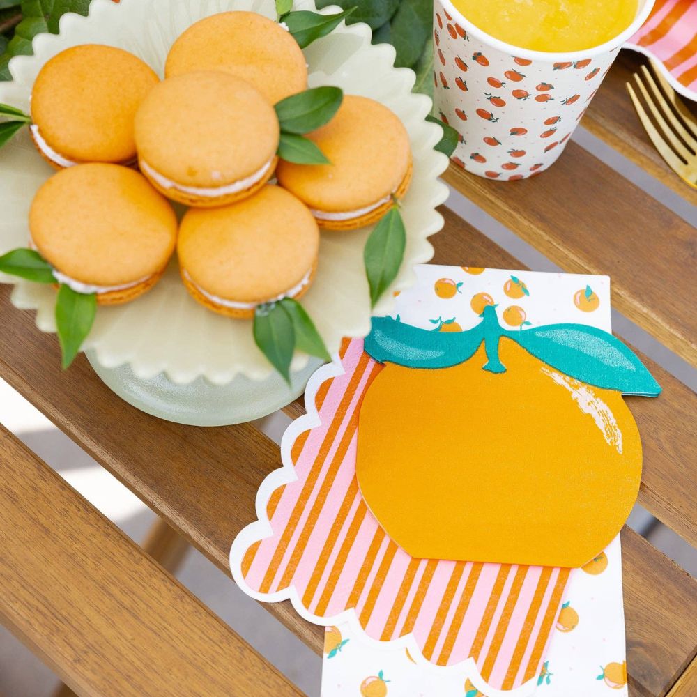 Orange and pink striped napkin styled with orange party plates and macarons.
