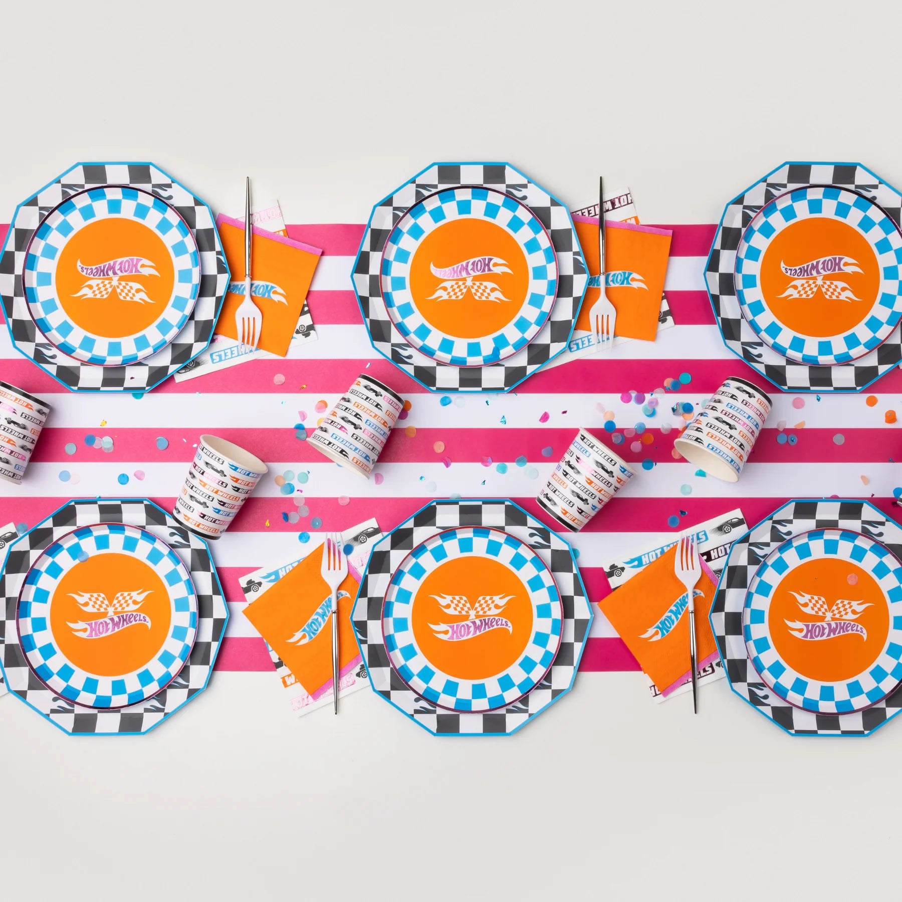 Overhead view of a party table setting featuring the hot wheels party supplies plates, cups, and race car napkins on a striped runner.