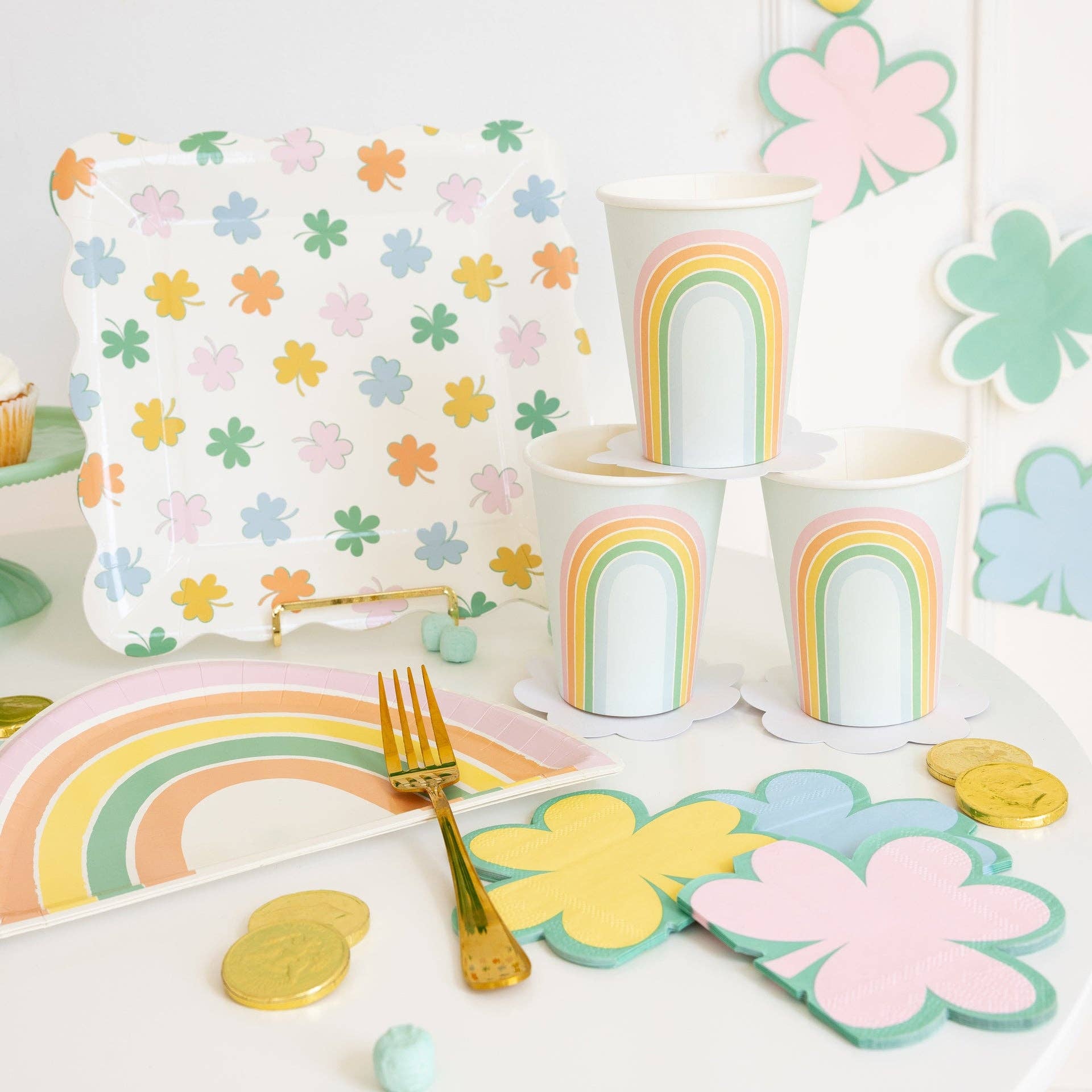 Pastel rainbow shaped paper plates styled on St. Patrick’s Day party table with shamrock decor