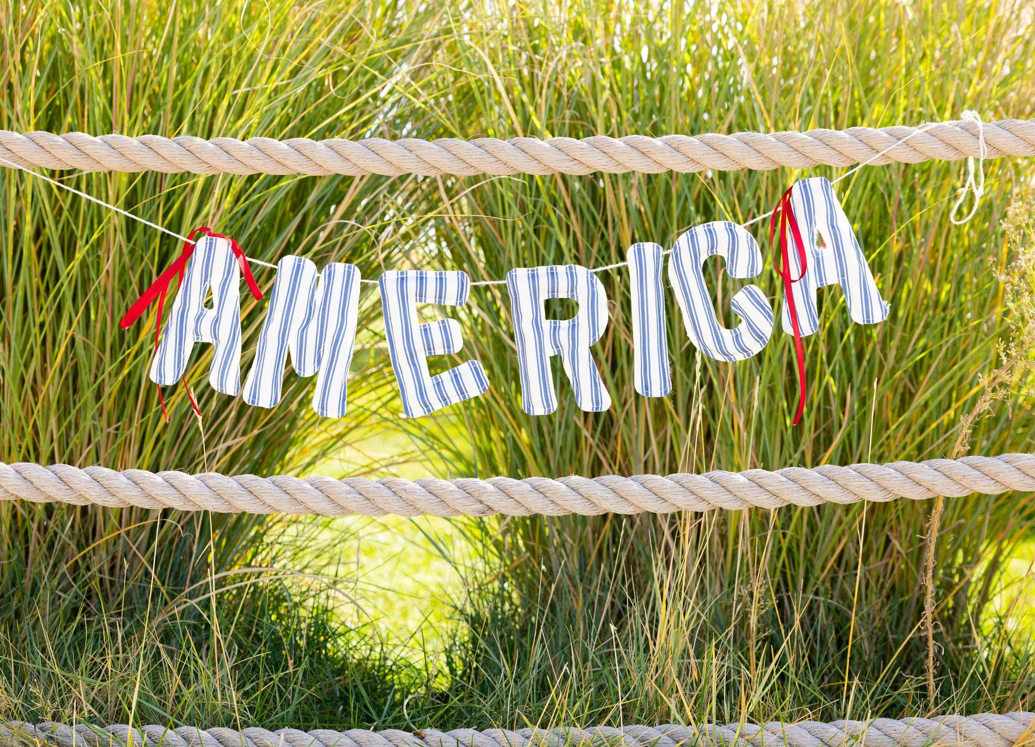 Patriotic America ticking stripe banner strung between rope fence posts with summer grasses behind