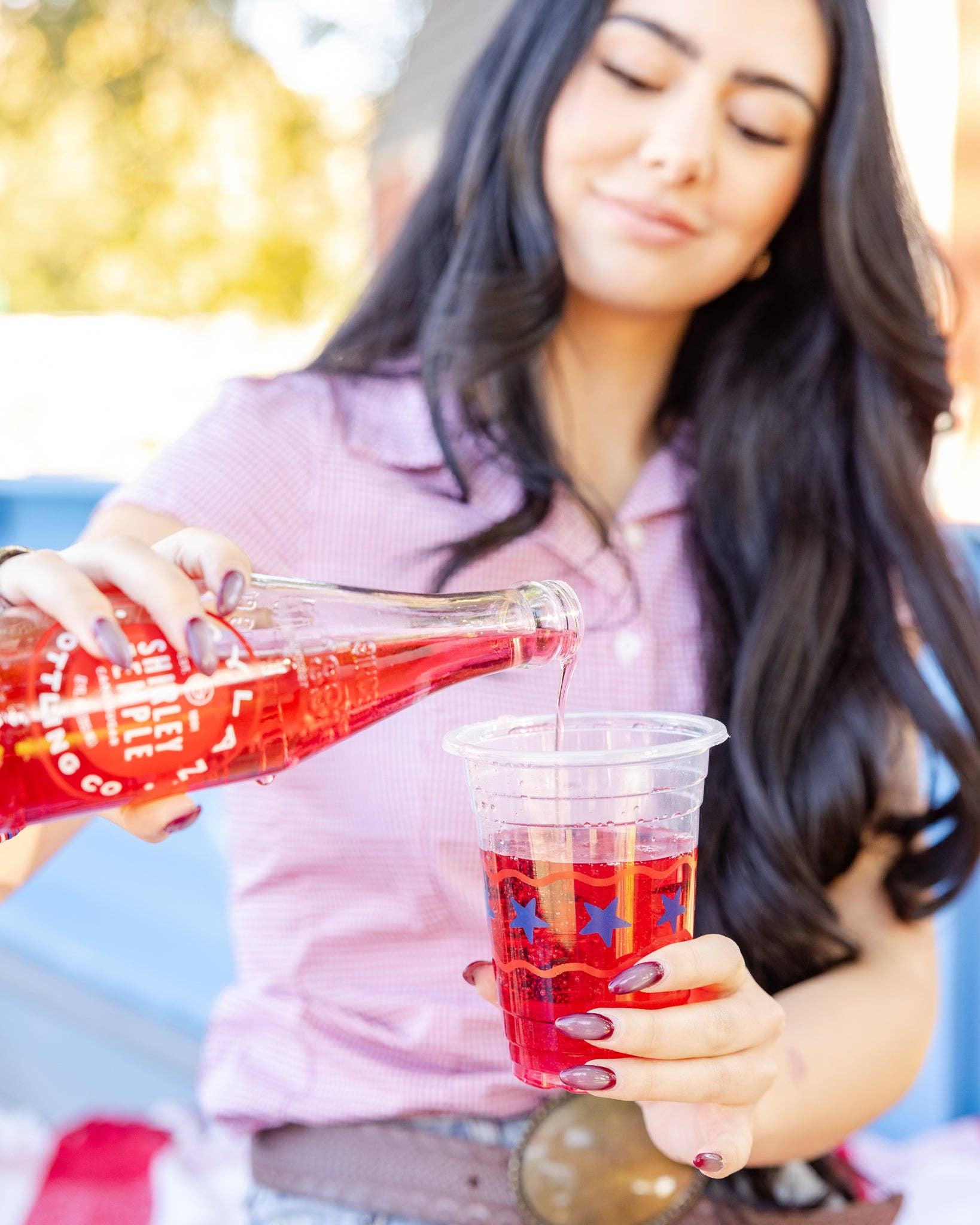 Close-up of woman pouring a drink into a clear patriotic party cup with blue star and red stripe design