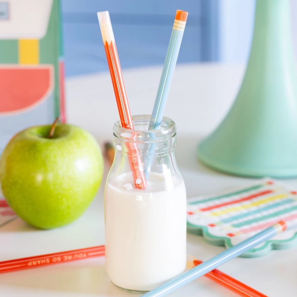 Pencil straws in glass milk bottle with apple and party setup.