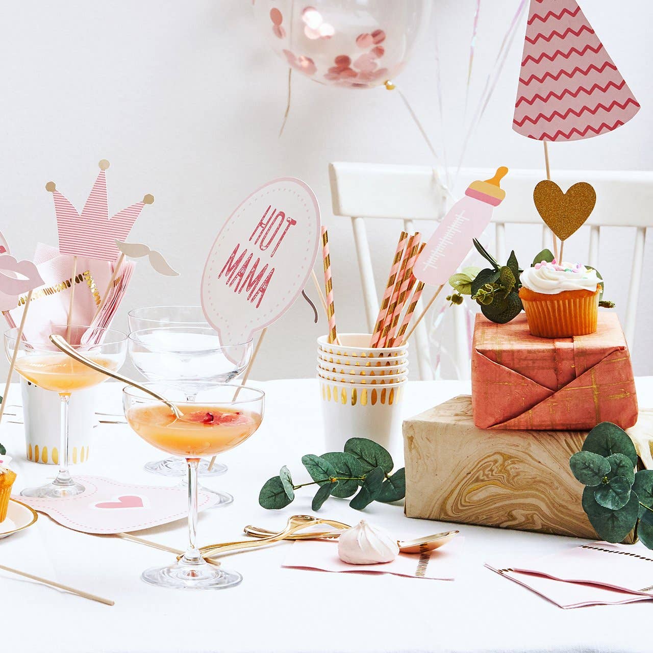 Aesthetic pink and gold baby shower drink station with striped paper straws, champagne coupes, and "Hot Mama" party props.