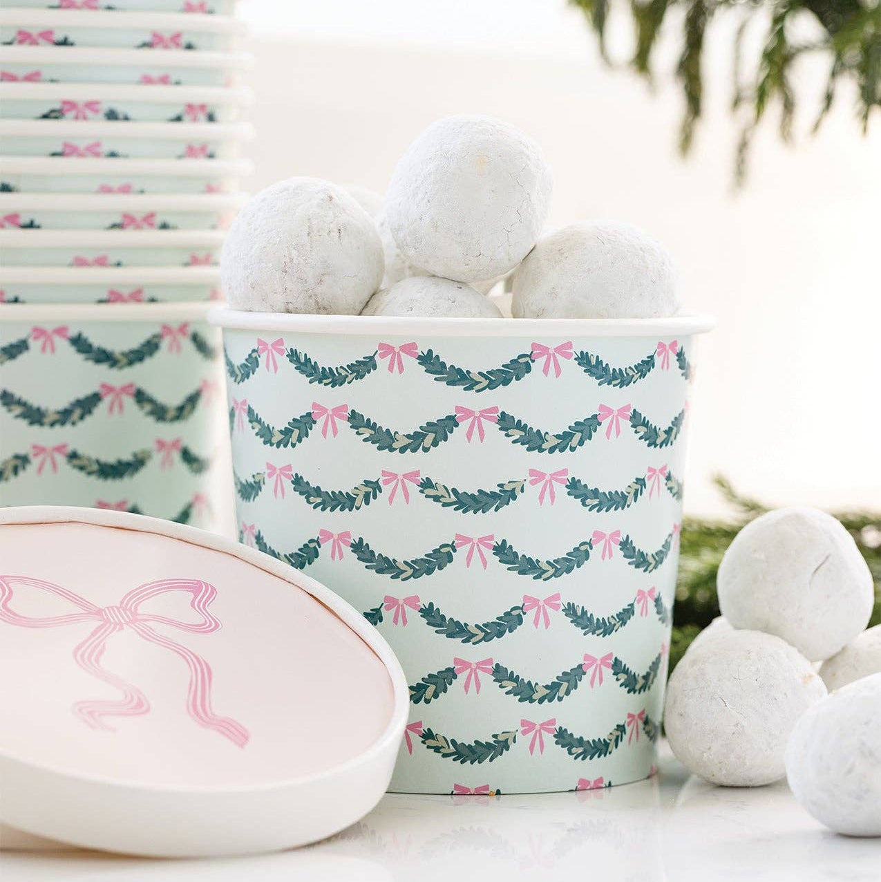 Pink bow treat cups filled with powdered donut holes on a styled party table.