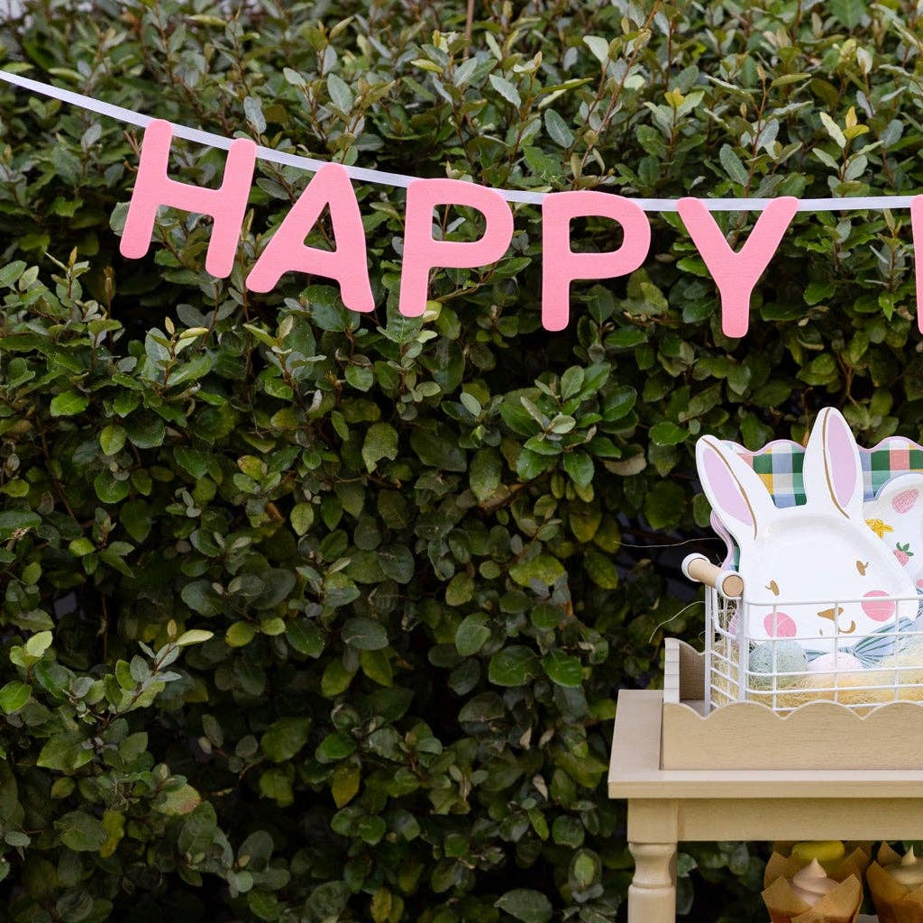 Close-up of pink felt HAPPY banner hanging outdoors above Easter setup