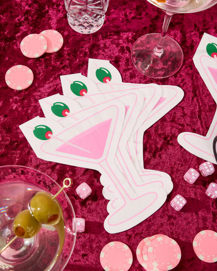 Pink martini napkins fanned on pink velvet tablescape with martini glass, poker chips, and dice