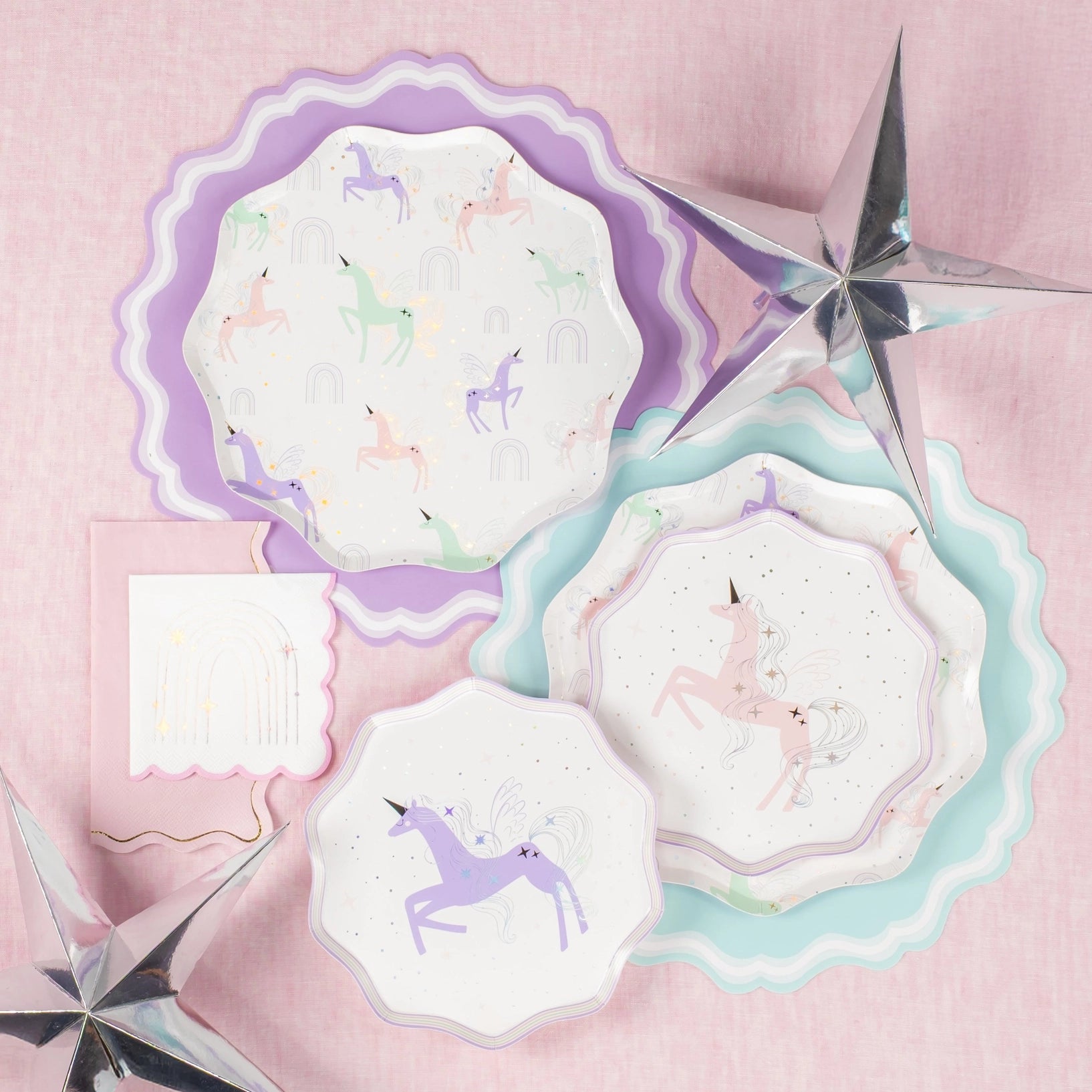 Flat lay: napkins beside layered pastel chargers and silver stars.