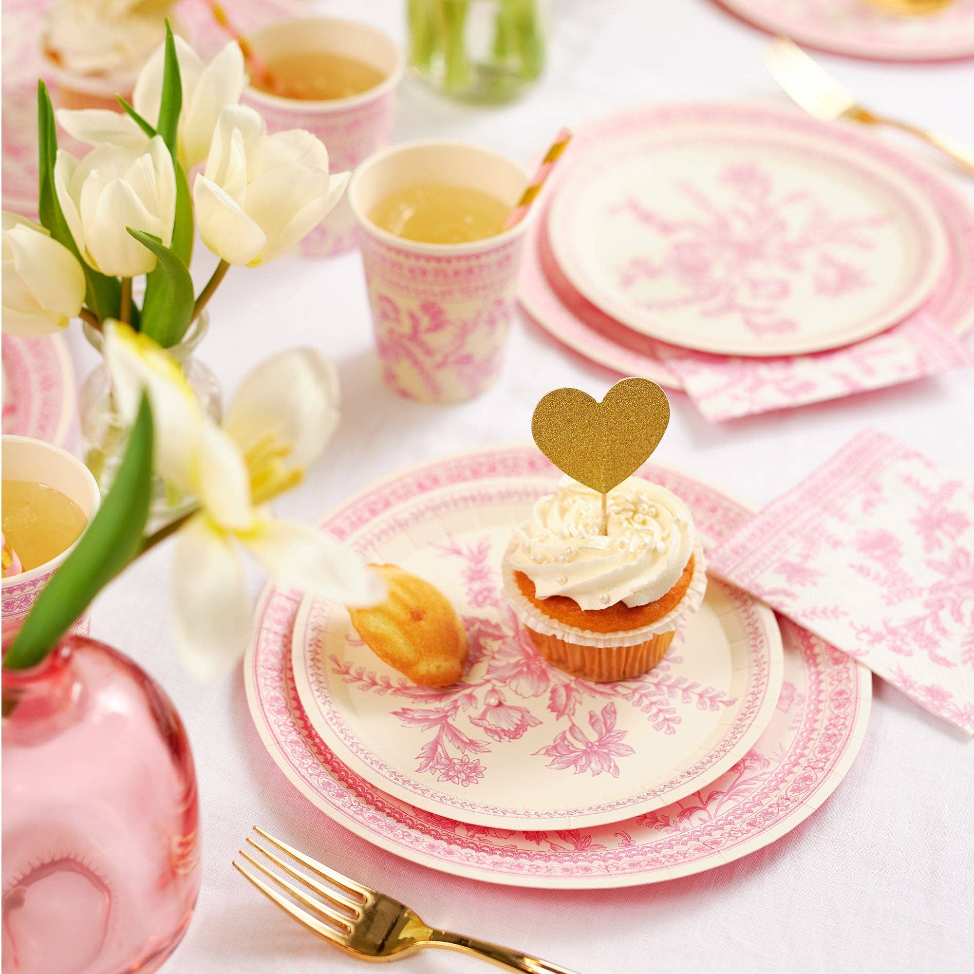 Tea party table setting with pink toile plates and cupcakes.