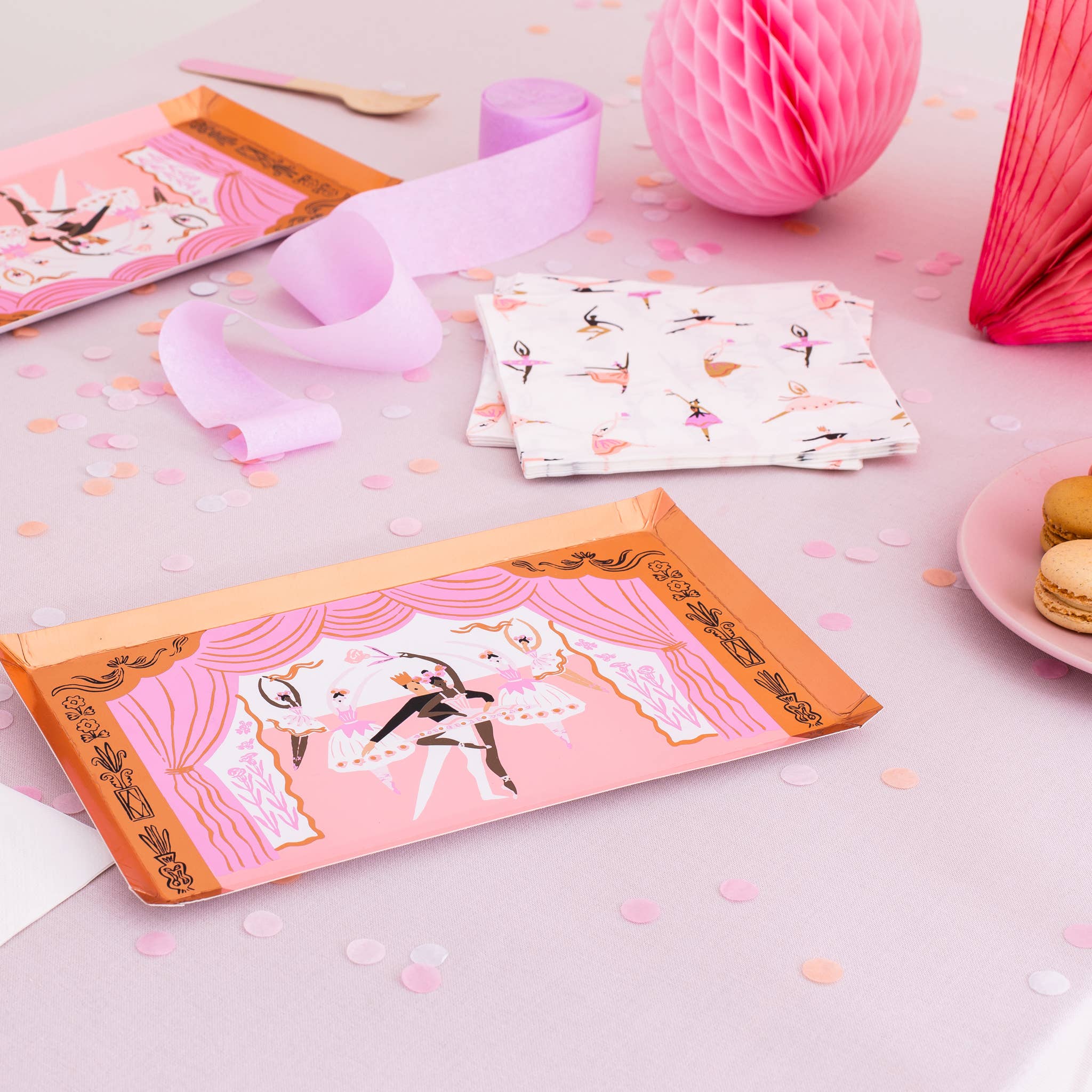 Flatlay of ballerina themed party supplies with pink tutu napkins, stage-shaped plates, and pink wooden forks.