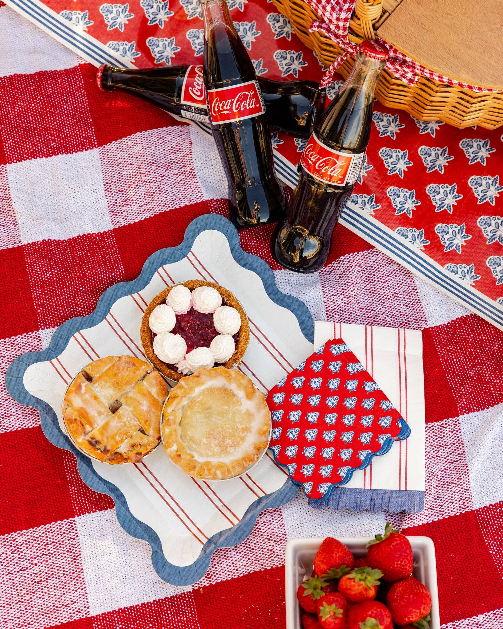 Red block print floral cocktail napkin and blue scalloped dinner plate with mini pies on red gingham picnic blanket