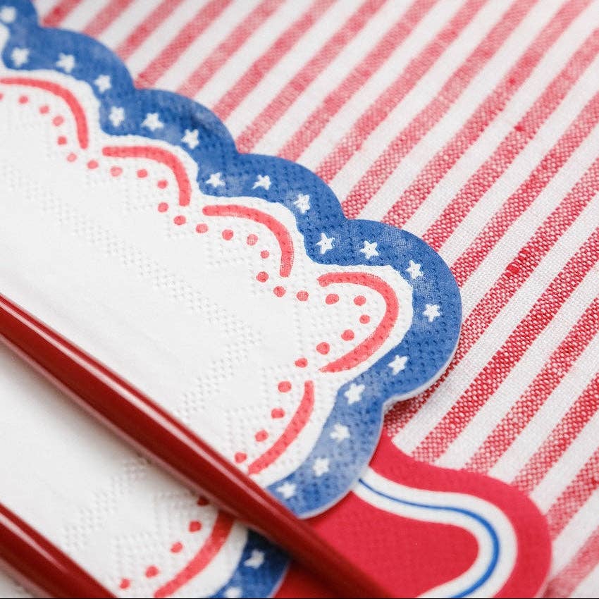 Close-up of a Watercolor Patriotic Party Decor napkin tucked under red utensils on a striped cloth.