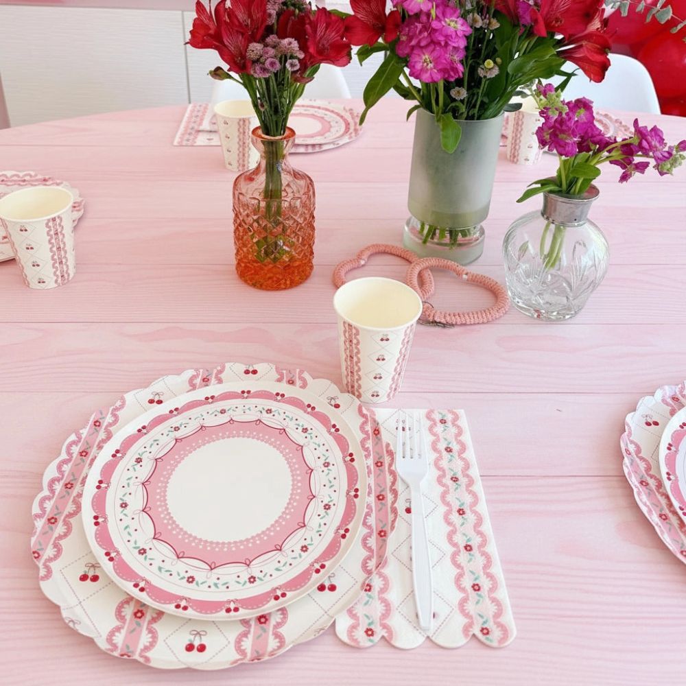 Cherry party setting on a pink table with matching cups and plates