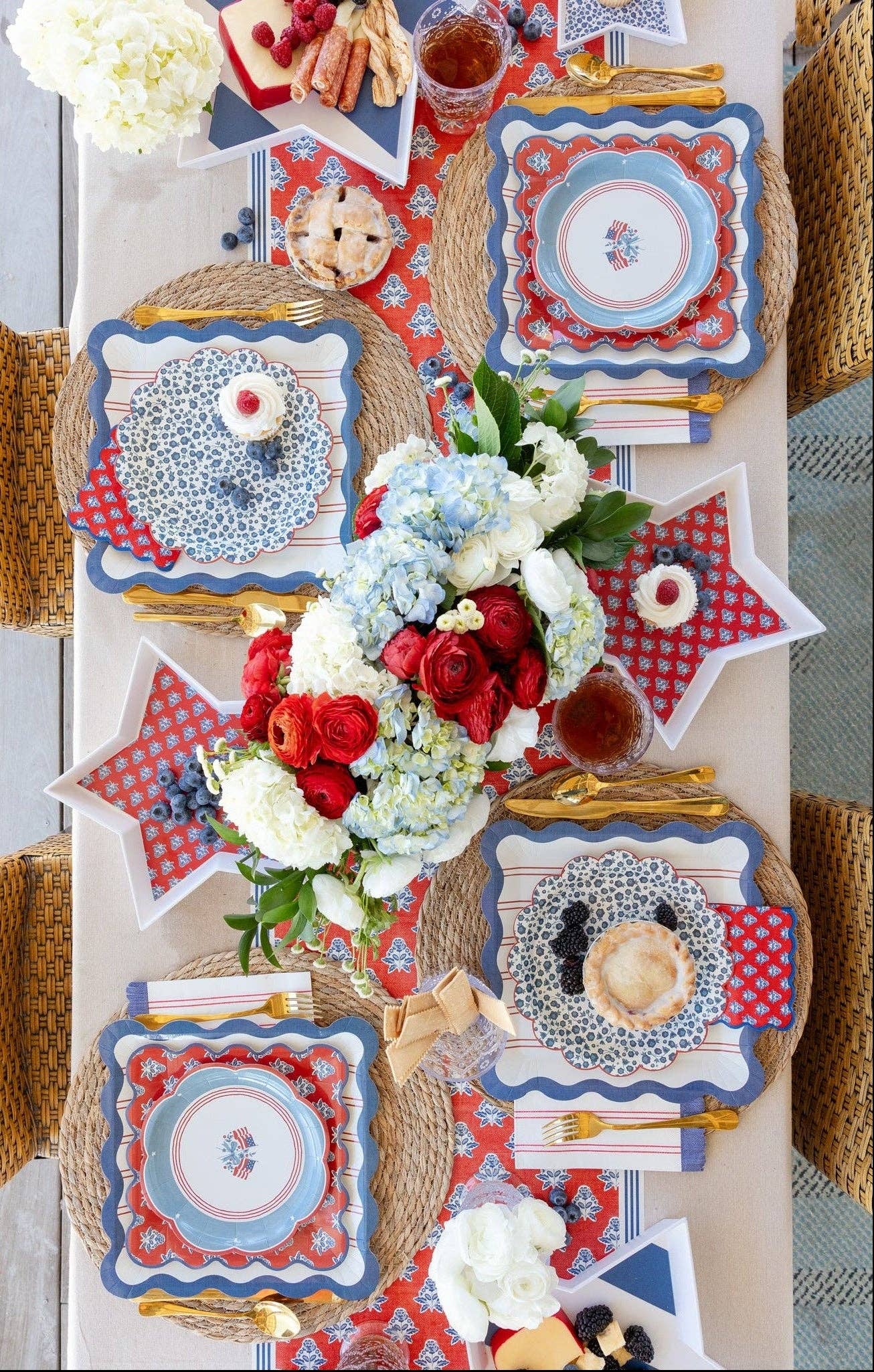 Full overhead view of Americana 4th of July tablescape with layered scalloped plates and red striped table runner visible beneath place settings