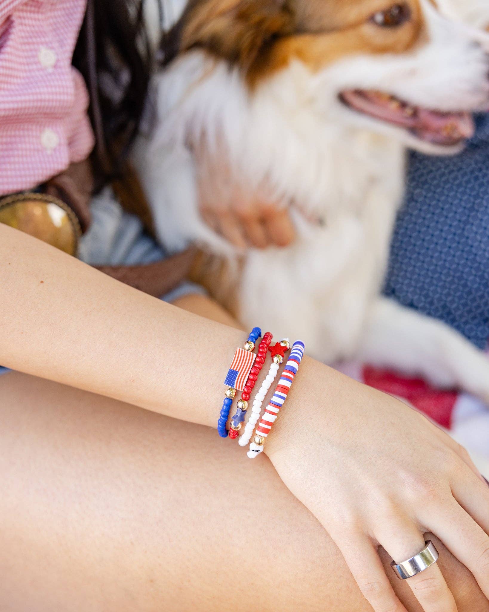 Close-up of four stacked red white and blue beaded bracelets with American flag charm, star charms, and USA letter beads on a woman's wrist