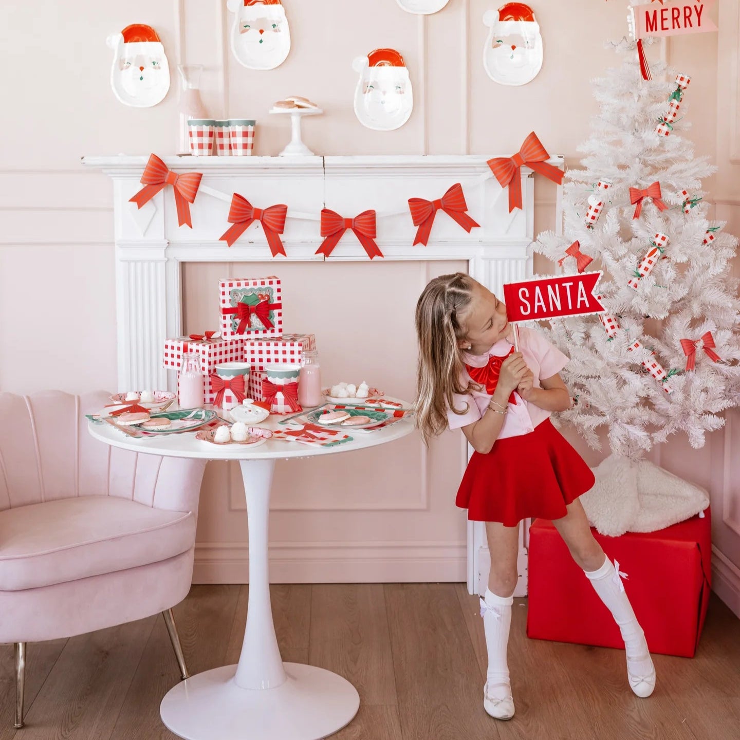 hild holding Santa felt pennant next to a white Christmas tree—cute Christmas party props.