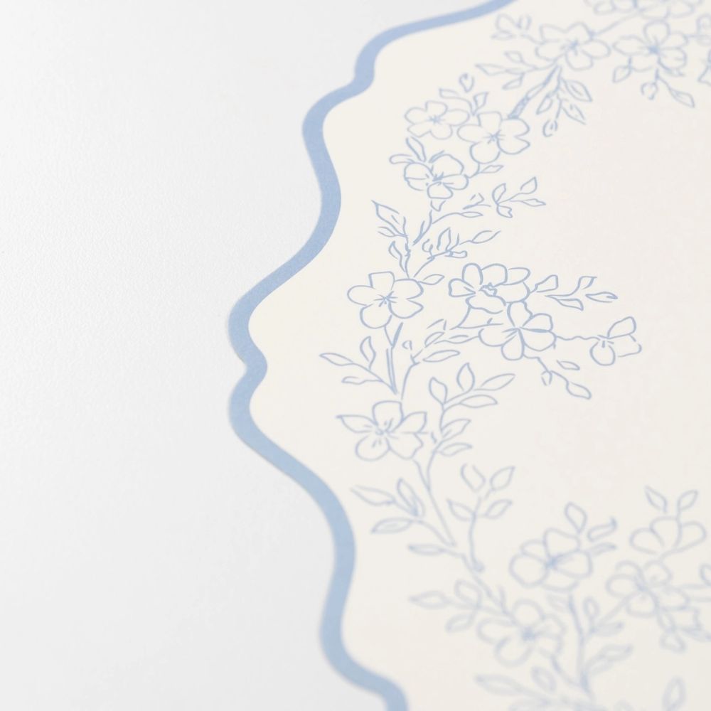 close up of scalloped edge on blue botanical paper placemat.