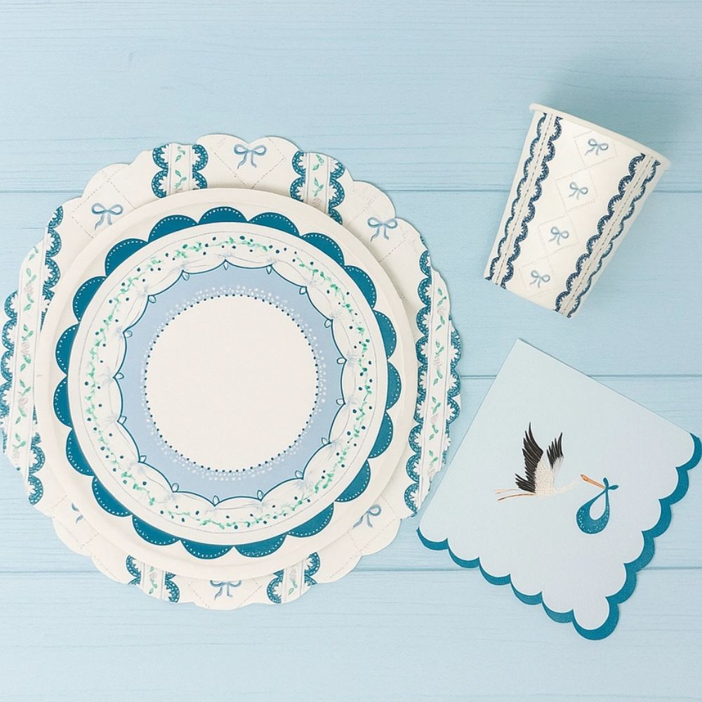 Place setting featuring a blue stork napkin next to stacked scalloped plates