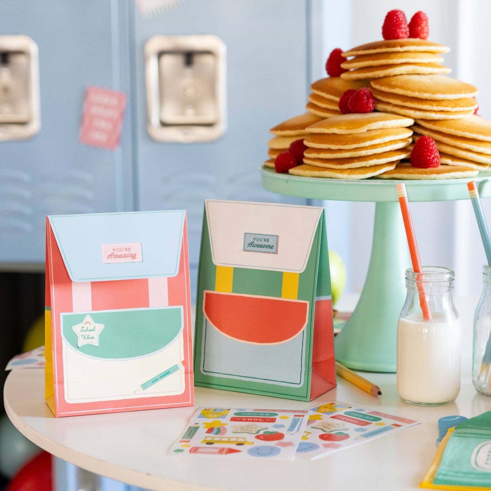 Two backpack treat bags displayed on table with pancakes and school-themed setup.
