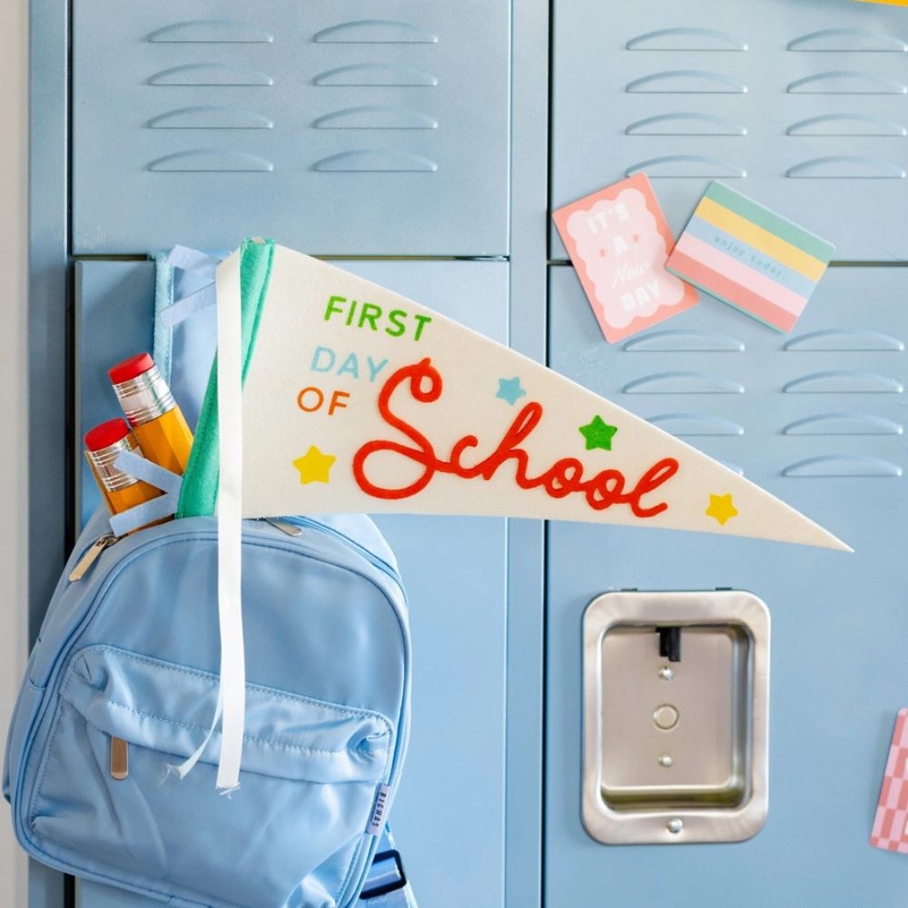 School pennant displayed on backpack in front of lockers.