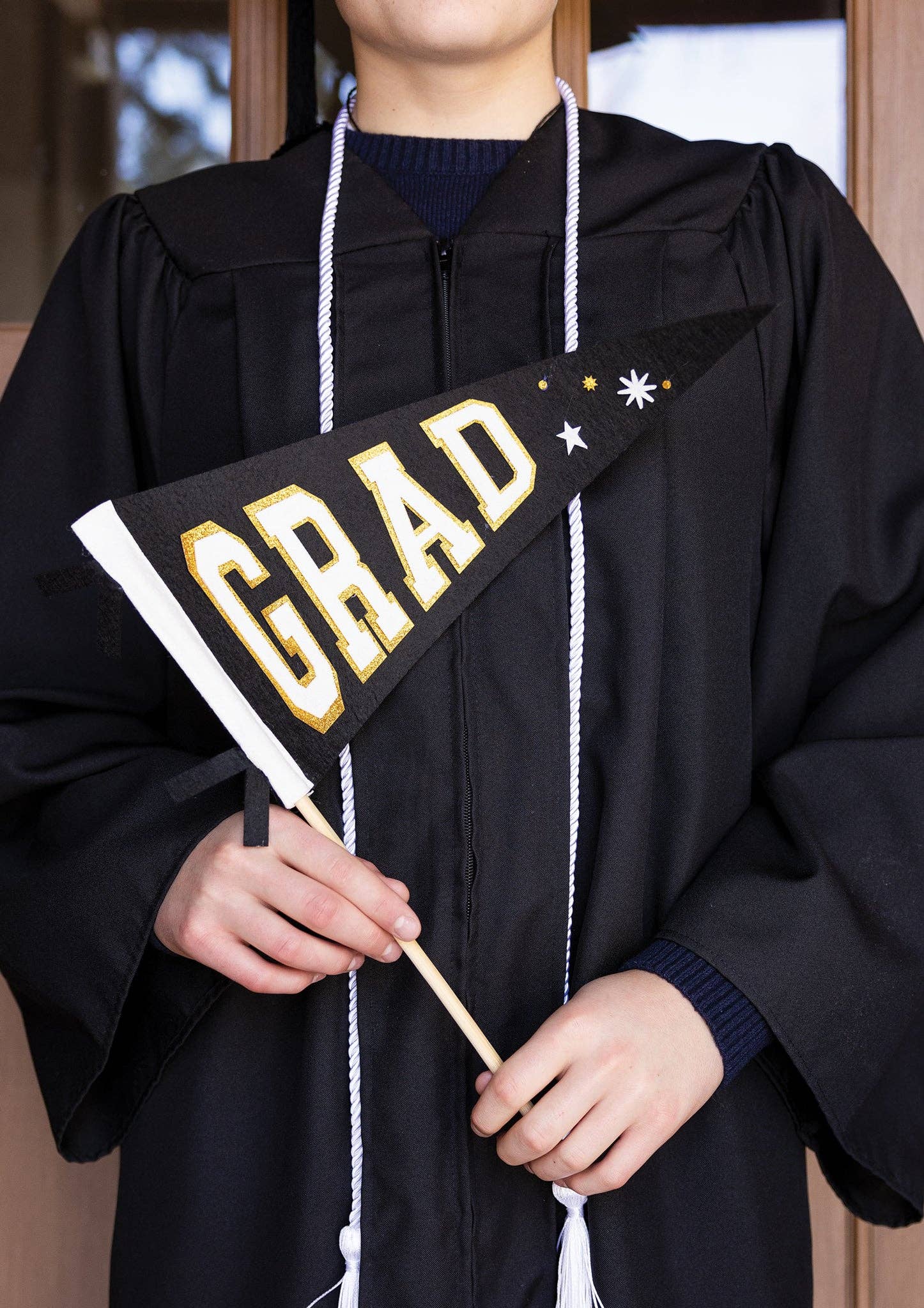 A graduate holding a black and gold felt graduation pennant as a matte, no-glare photo prop.