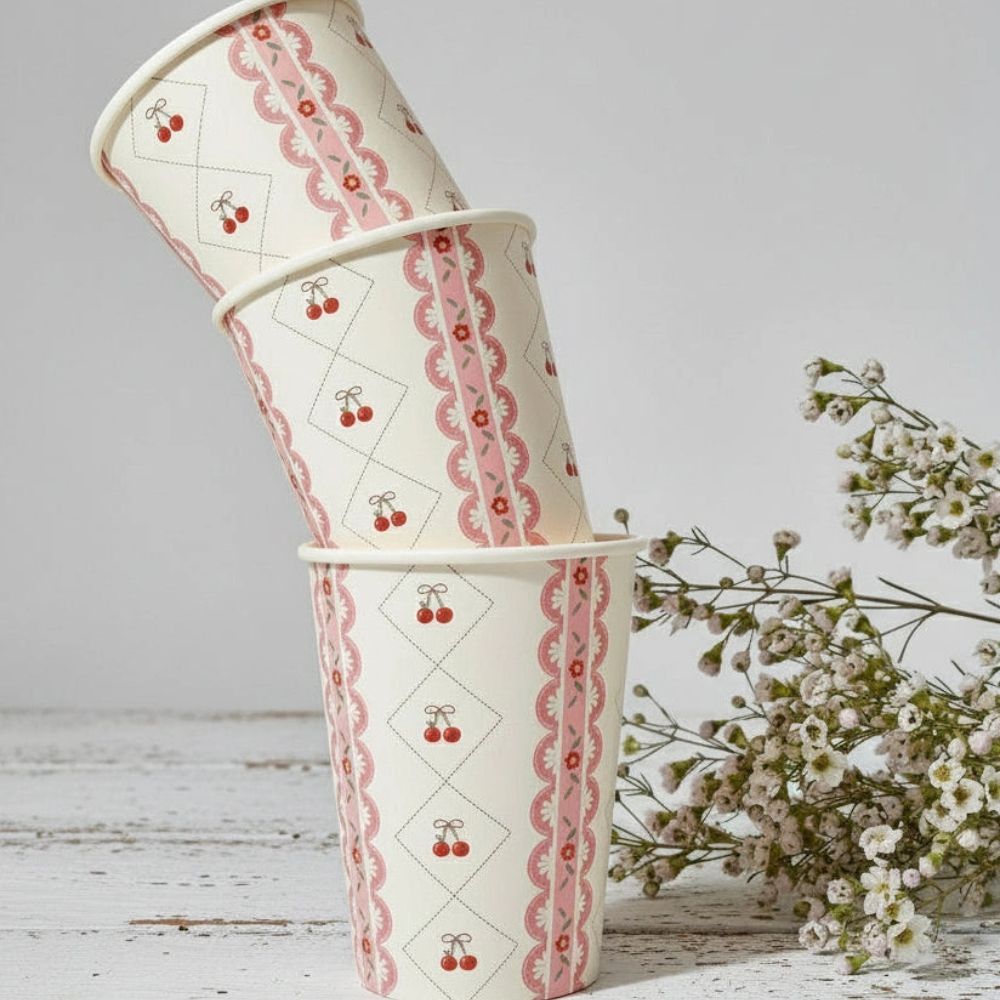 A stack of three cherry themed paper cups next to white wildflowers